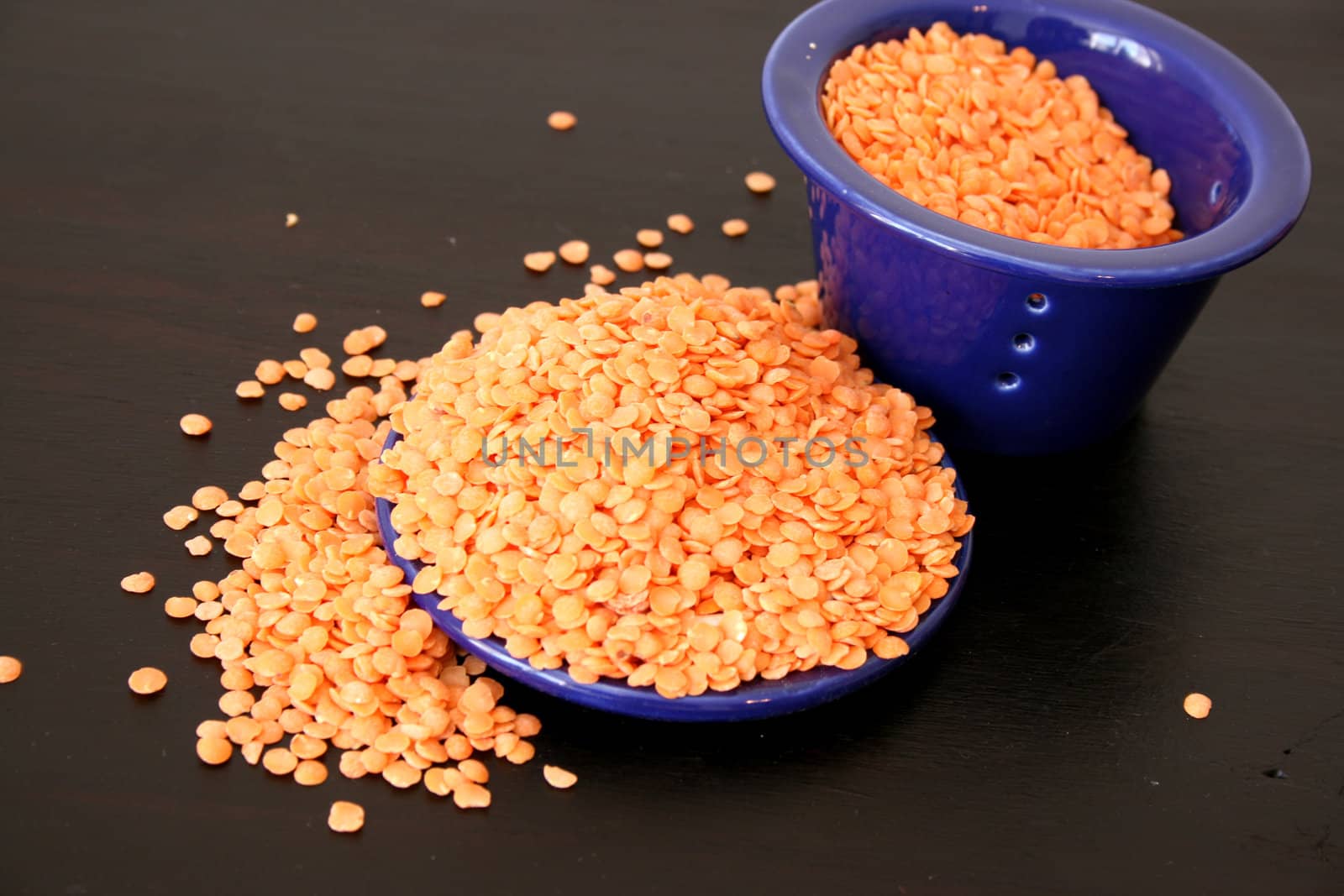 Lentils overflowing from blue ceramic bowl on a brown surface
