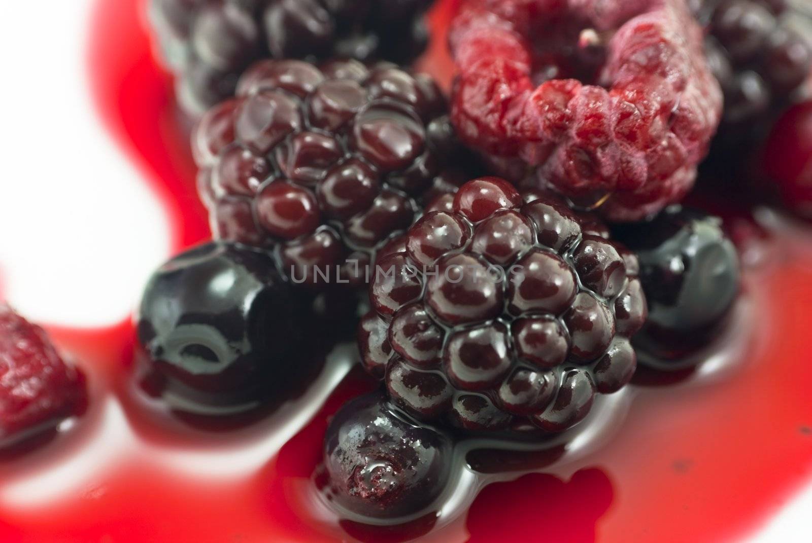 Closeup of Summer berry fruits on a white plate, bathed in natural berry juice.  Includes blackberries, raspberries, blackcurrants and redcurrants.