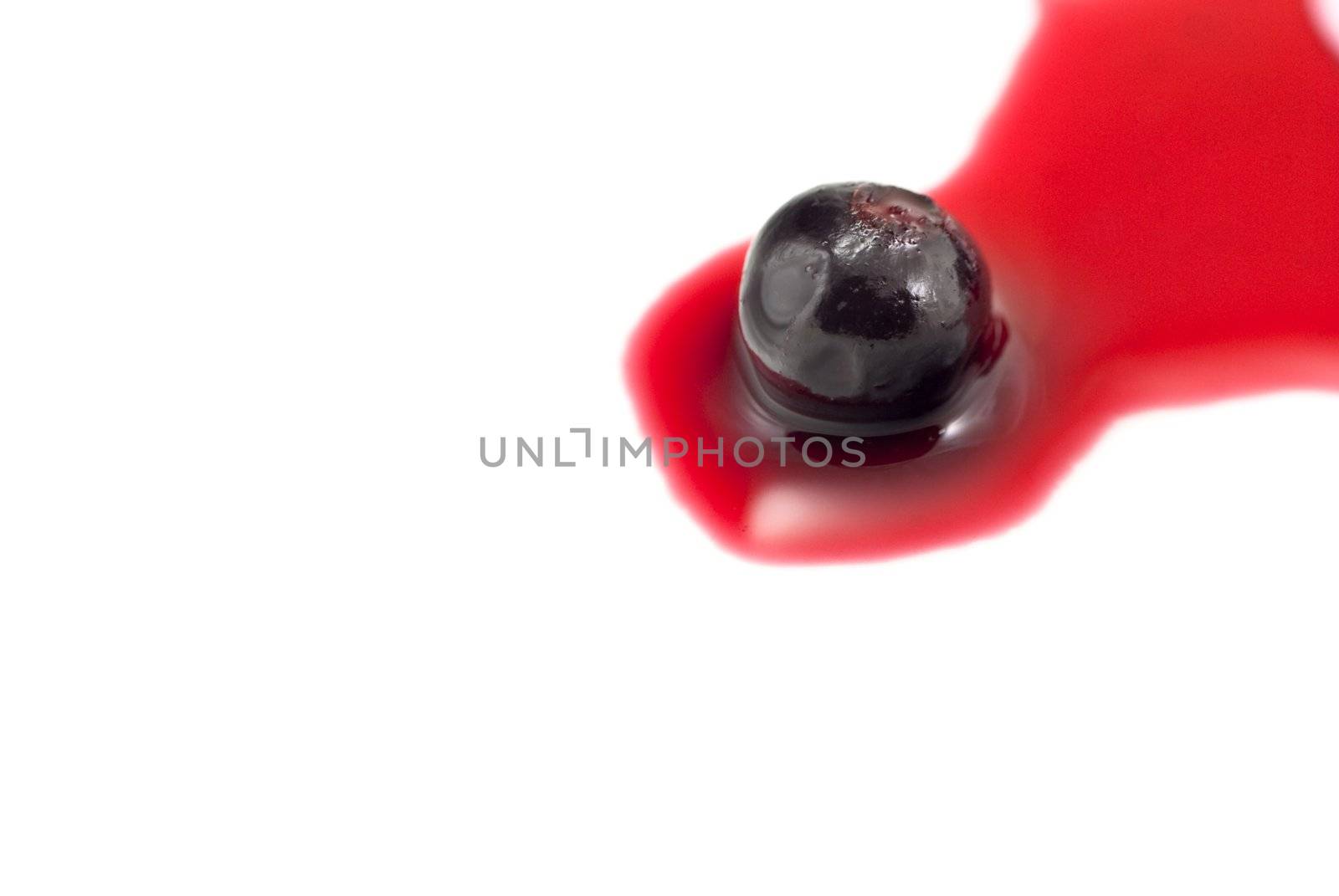 Close-up of a solitary blackcurrant in redcurrant juice, isolated on white background.  Seated on right side of frame with copy space to the left.