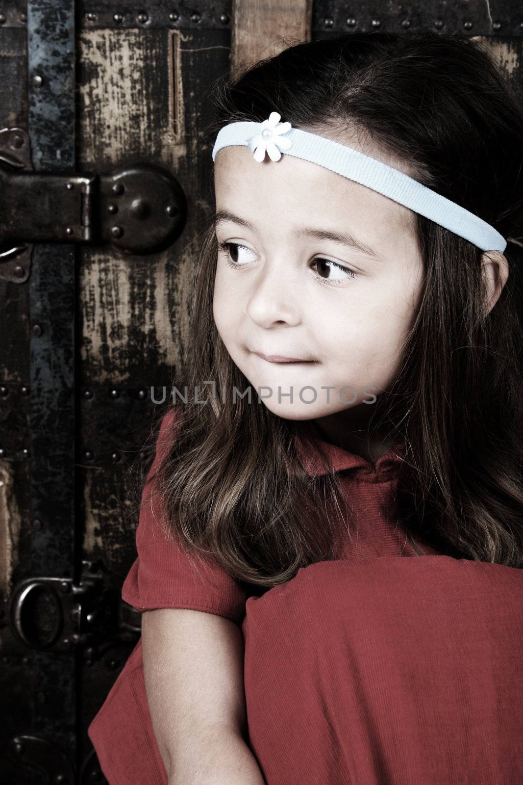 Cute brunette girl sitting against an antique trunk wearing a headband