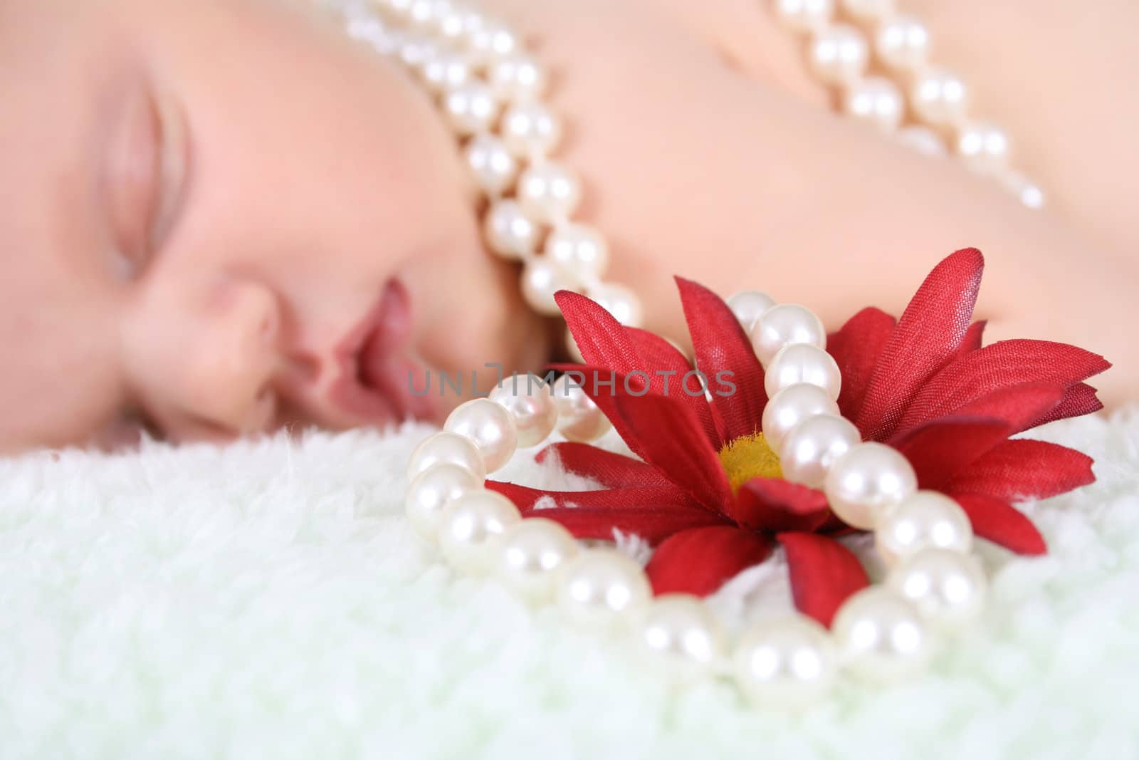 Beautiful baby girl sleeping, pearls draped with flower.  FOCUS ON FLOWER AND PEARLS.