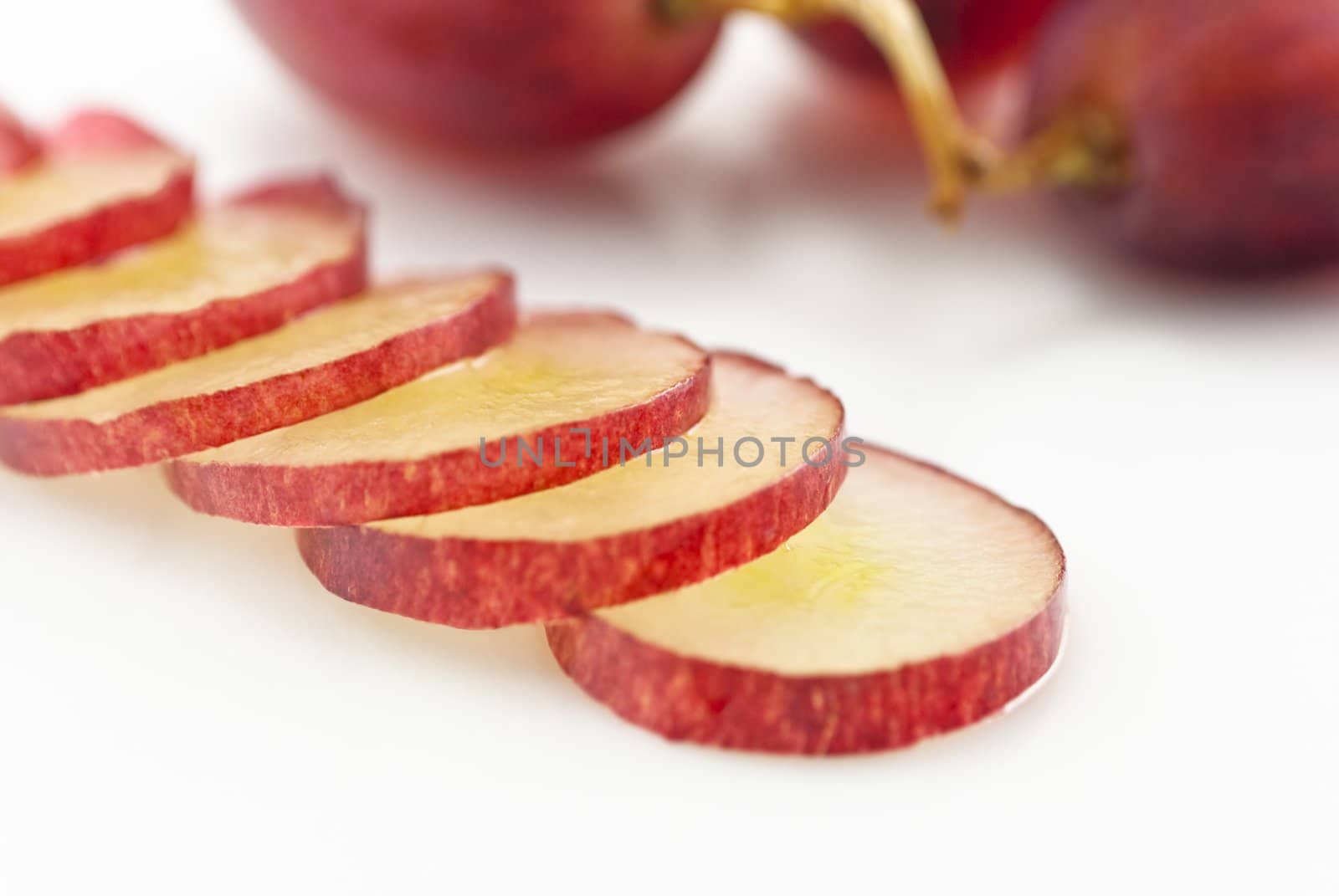 Close-up of red grape slices in the foreground, lying diagonally across a white china plate.  Three grapes connected by a stalk in soft focus in the background.