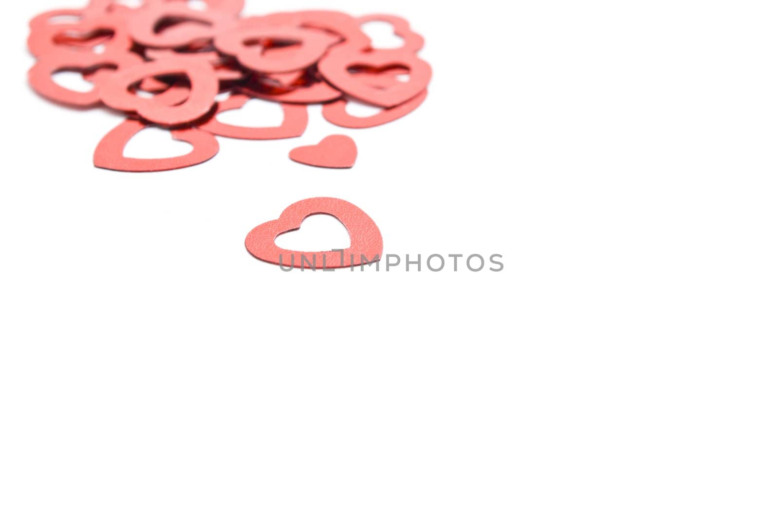 Decorative red hearts, scattered on a white surface.  Focal point is heart in foreground.  