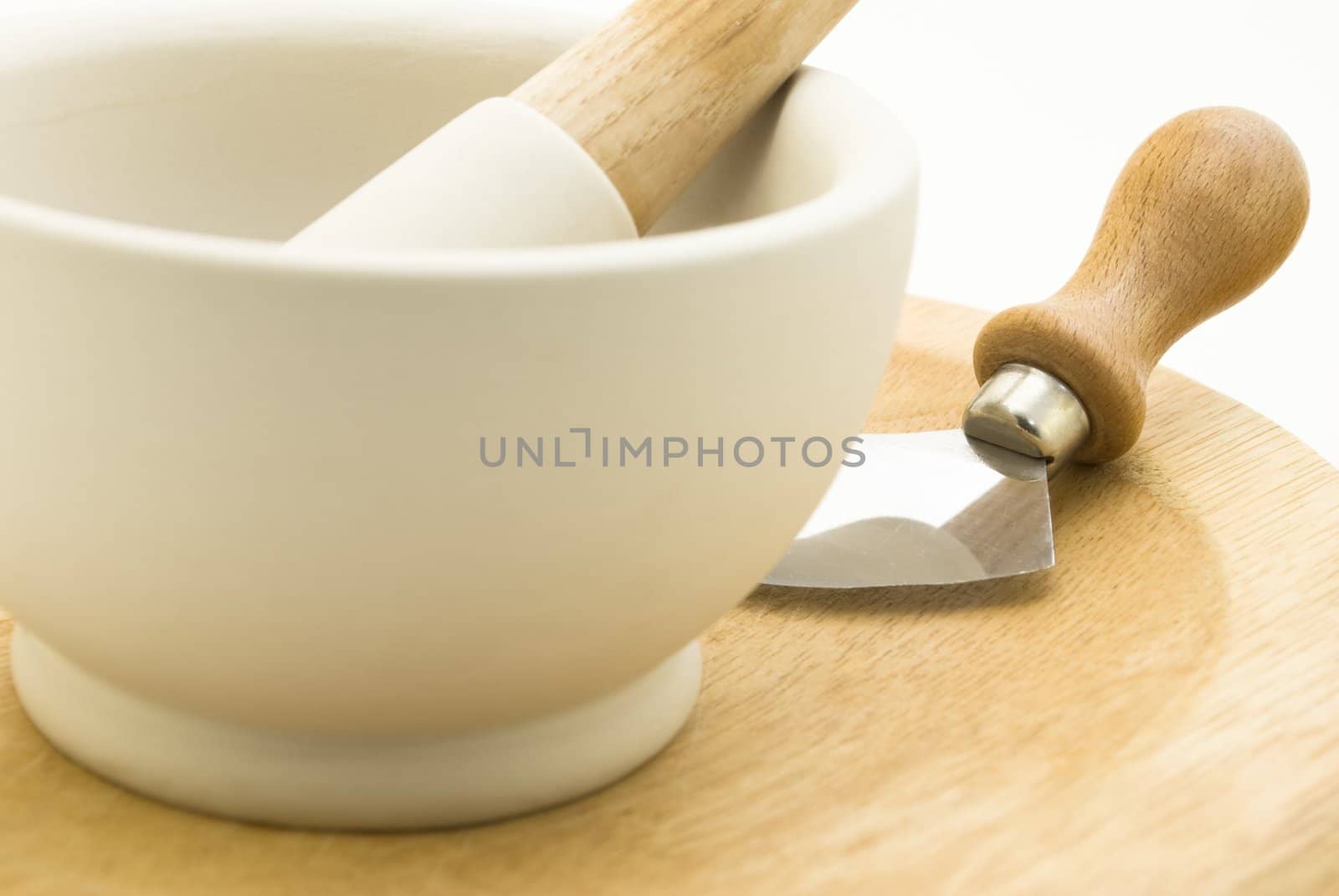 Close up of a cream stone pestle and mortar standing on a wooden mezzaluna chopping board with blade.  White background.