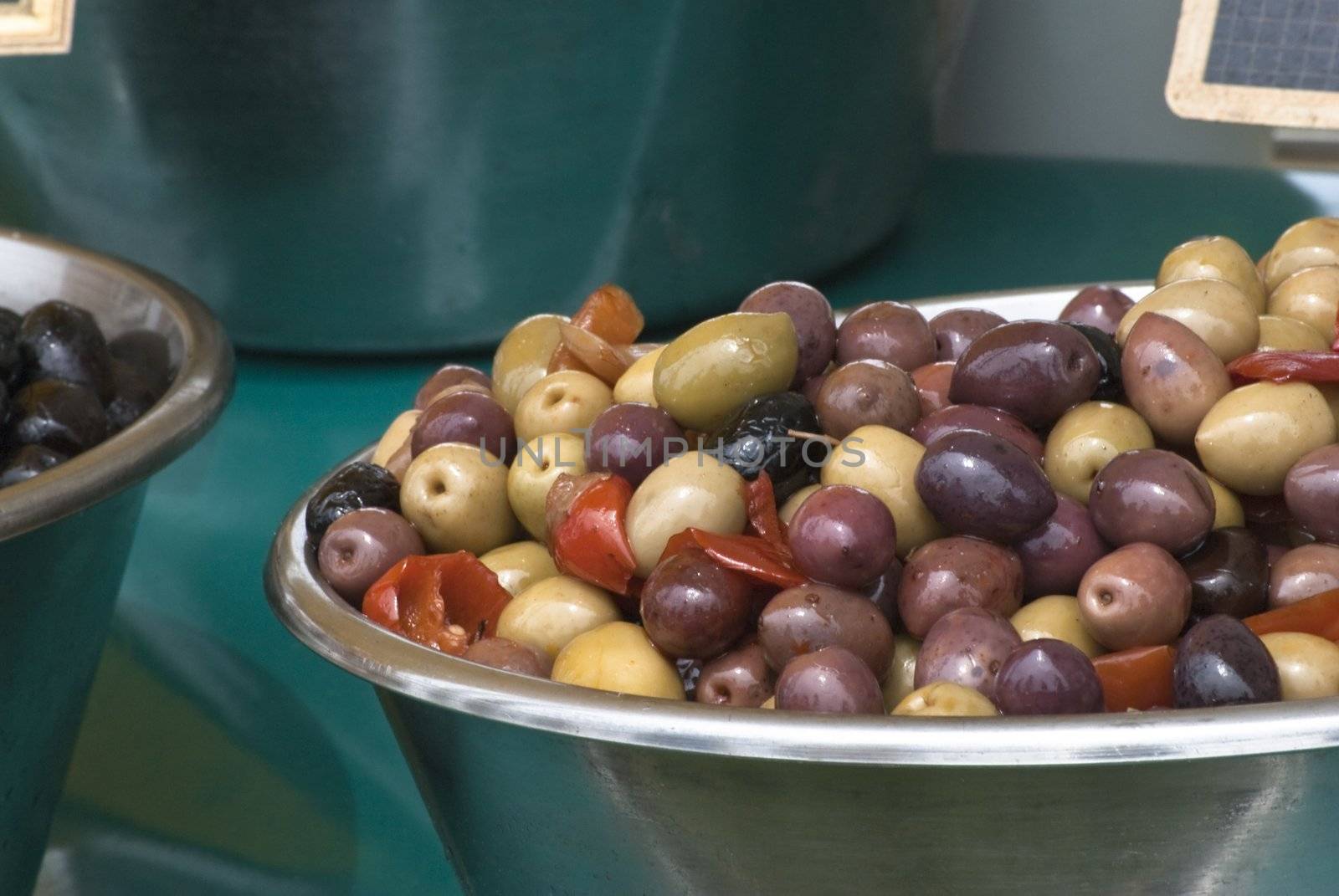 Two bowls of olives in foreground, one mixed and one black.  Sitting on a teal tablecloth on an open market stall.