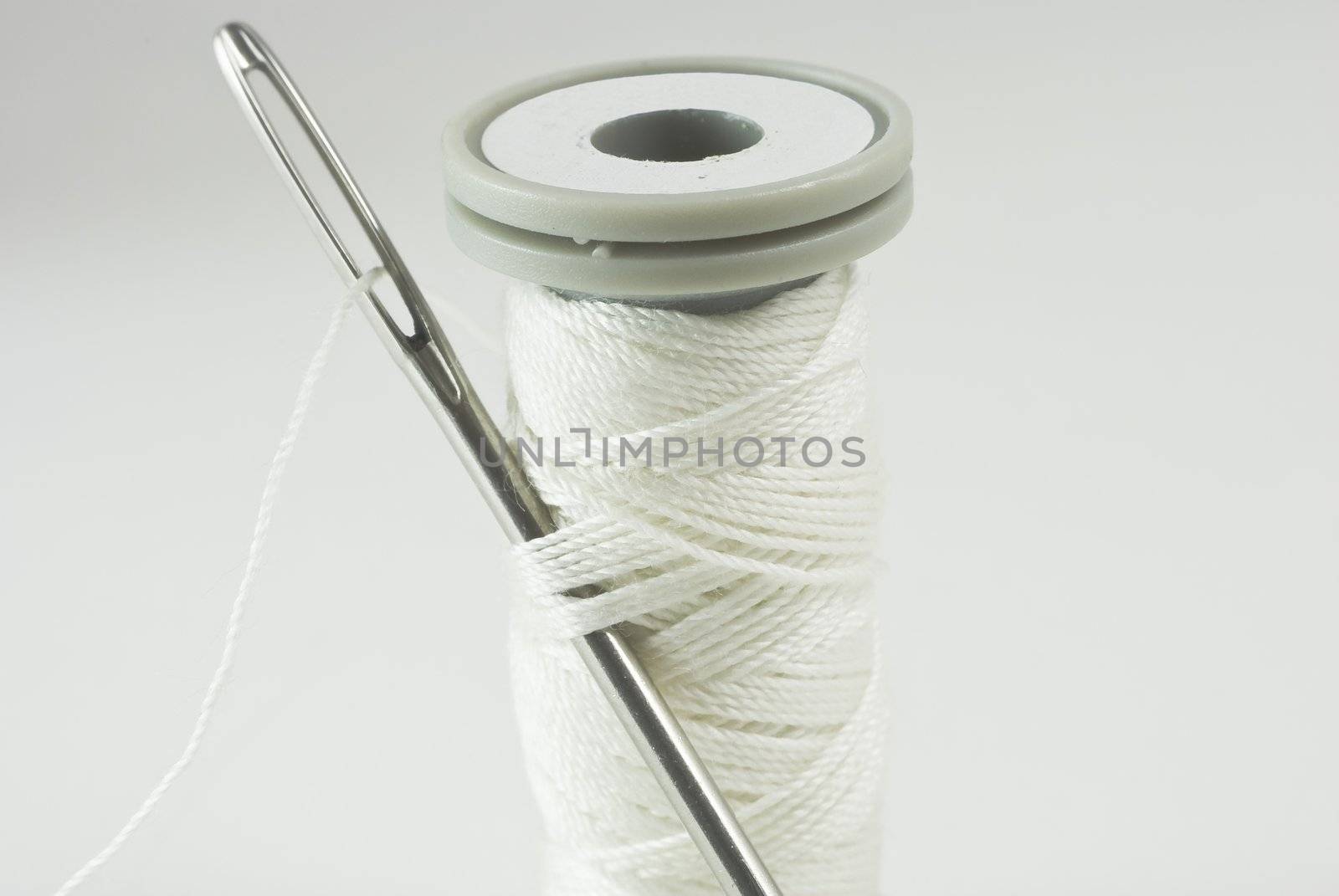 Sewing needle threaded with white cotton, inserted into thread on cotton reel.