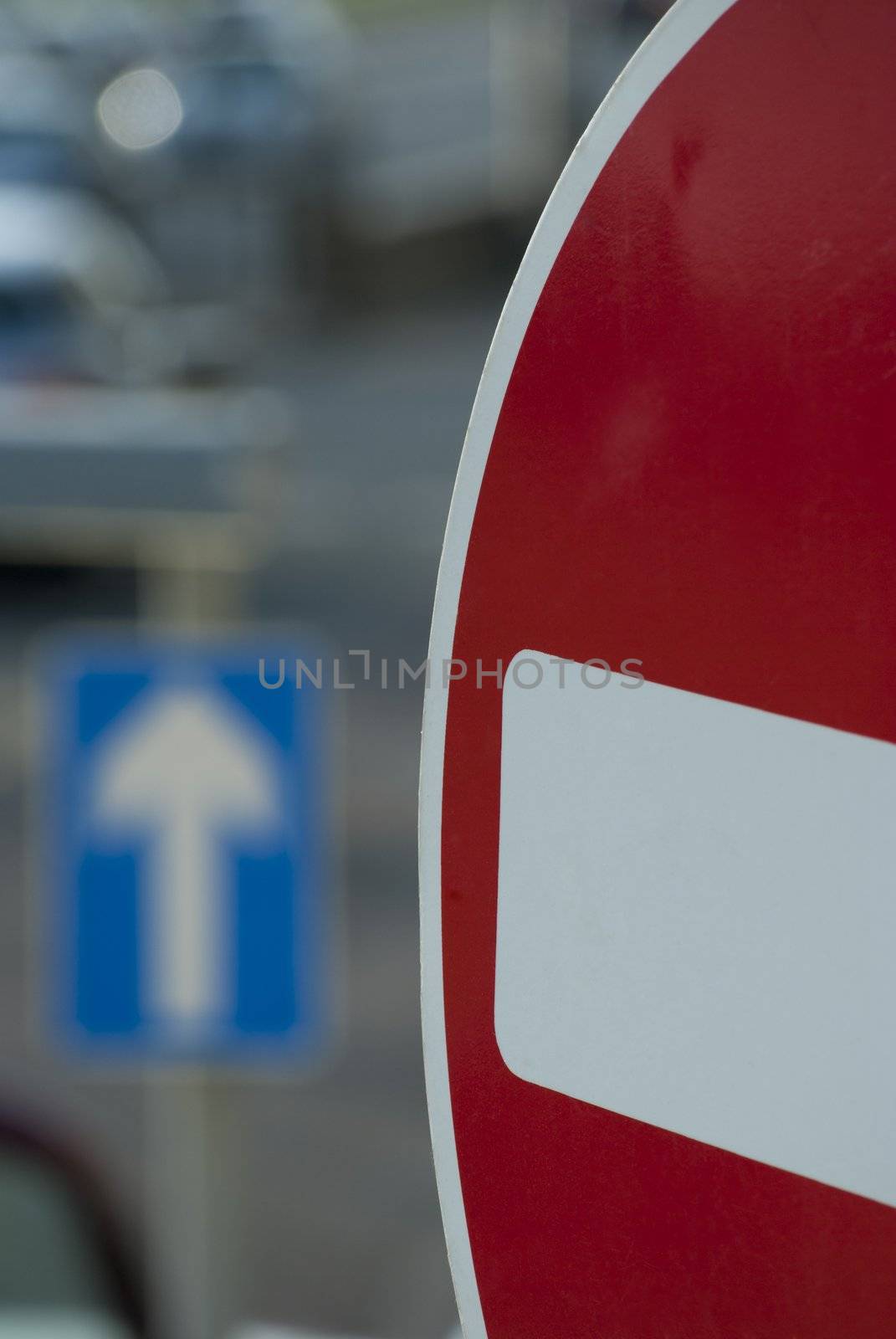 Traffic scene in a UK city, showing closeup of no-entry sign in the foreground, with a one-way sign and traffic queue in soft focus in the background.