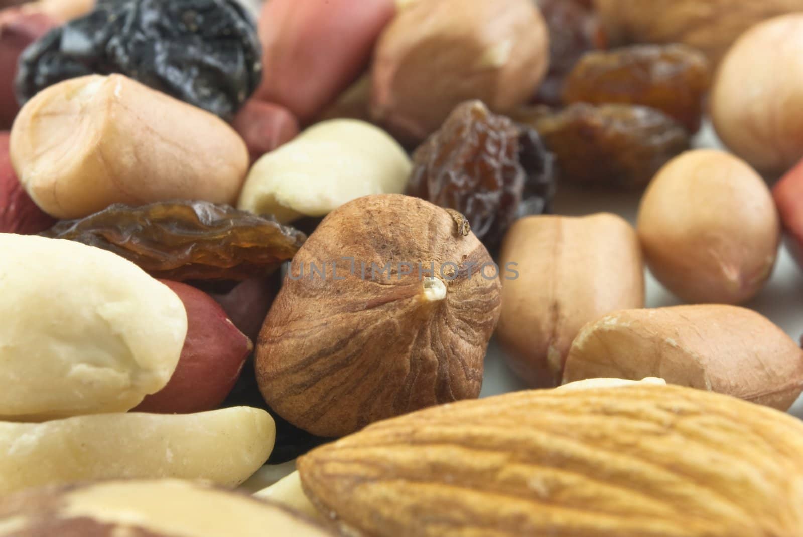 Close-up of mixed shelled nuts and raisins on a white plate.  Includes hazelnuts, peanuts, almonds and raisins.