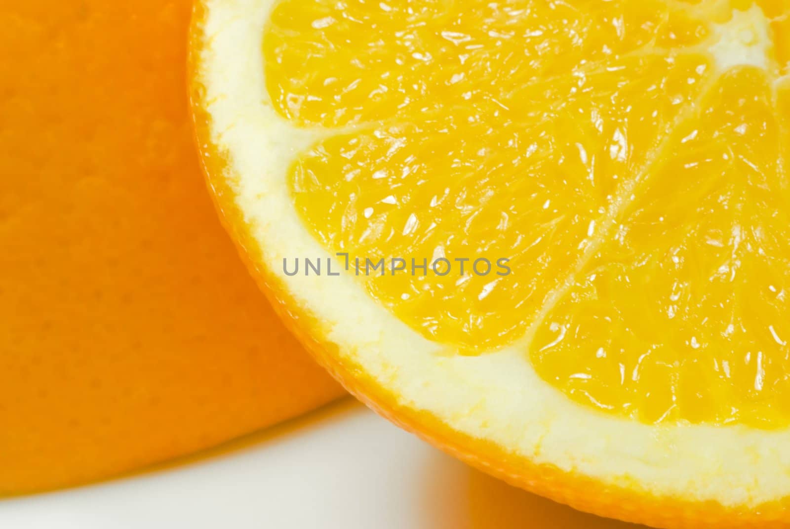 Close up (macro) of one slice of orange (quarter visible in foreground) leaning against upturned orange half, on white china surface with visible shadows.