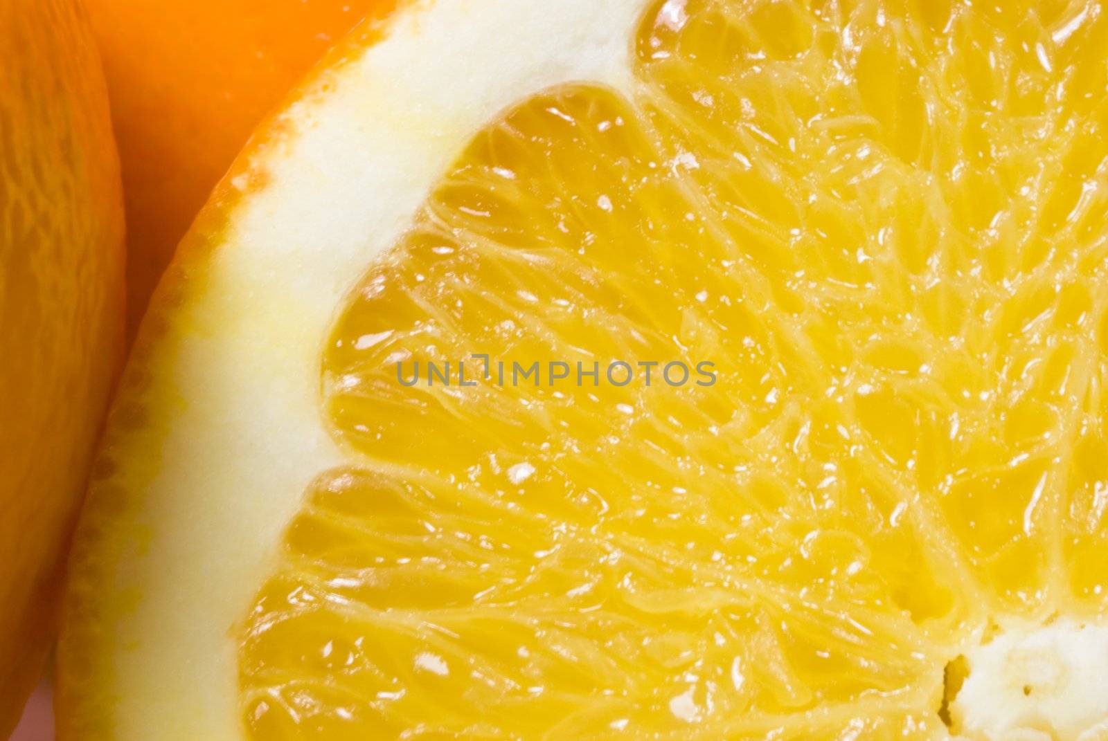 Close up (macro) of orange slice.  Top-left quarter of the slice almost fils the frame.  The peel of two other orange segments are visible to the left and back.  White surface is just visible in lower left corner of picture.