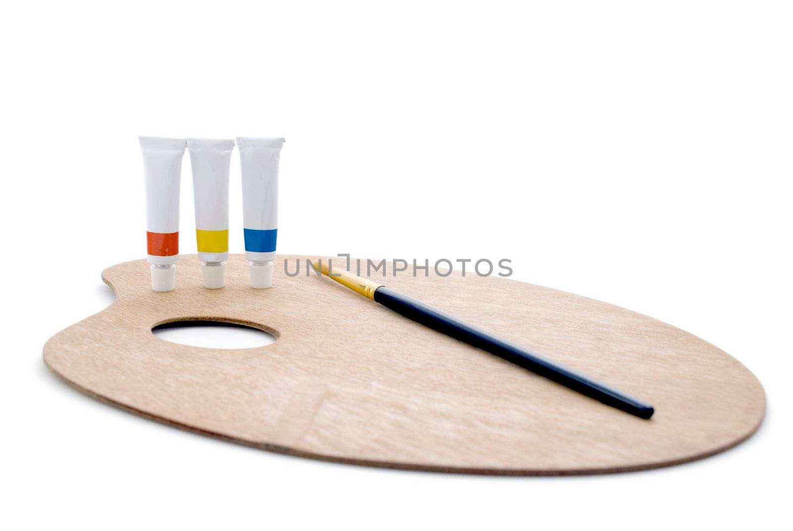 Three tubes of paint (primary colours) and a black/gold paintbrush, standing on a wooden artist's palette, isolated against a white background.  Shadows visible.  Whole composition in frame.