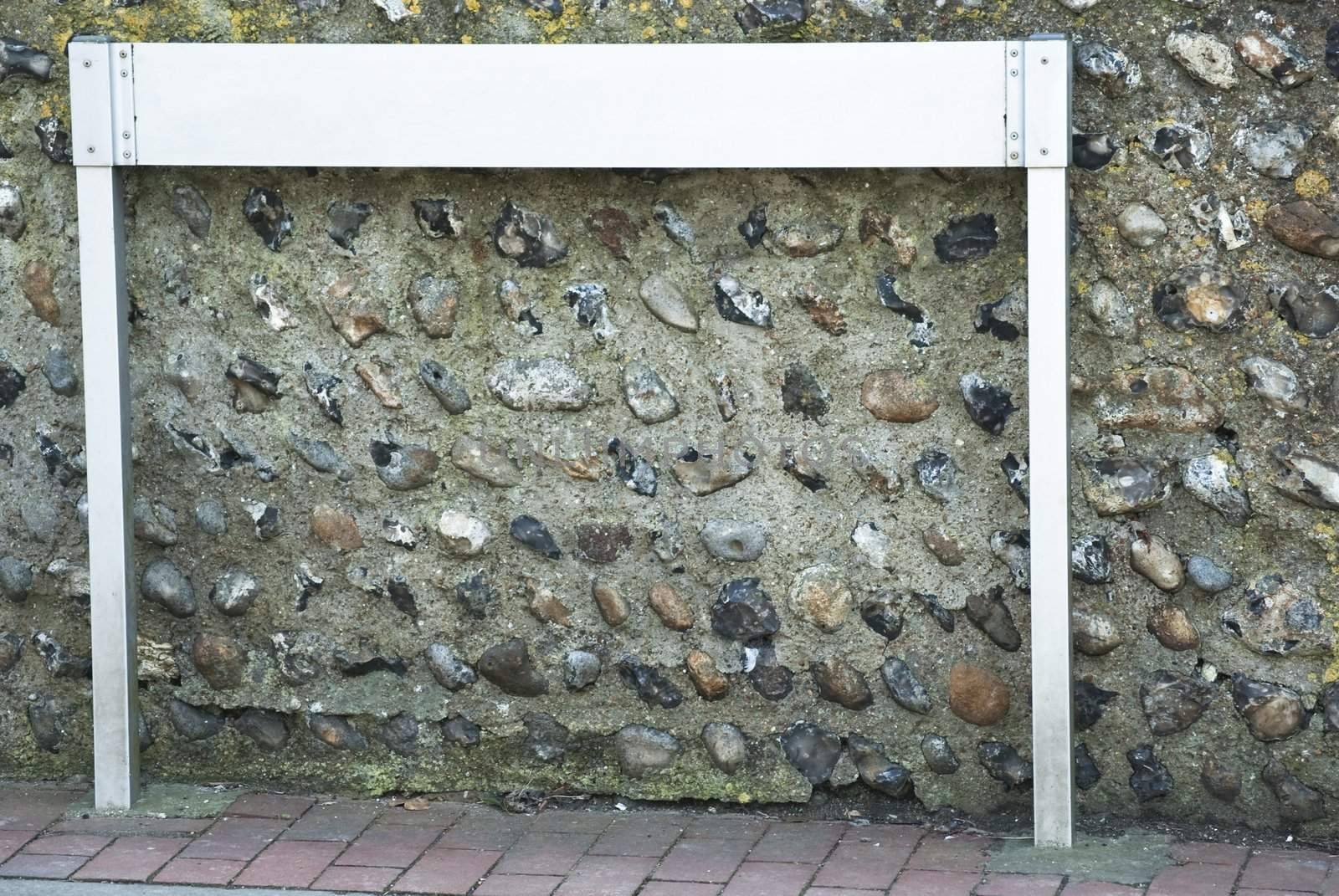 A white signpost in a village lane against a flint stone wall, on a brick work path.  Cleaned of text to provide copy space for the designer.  Kerb just visible.