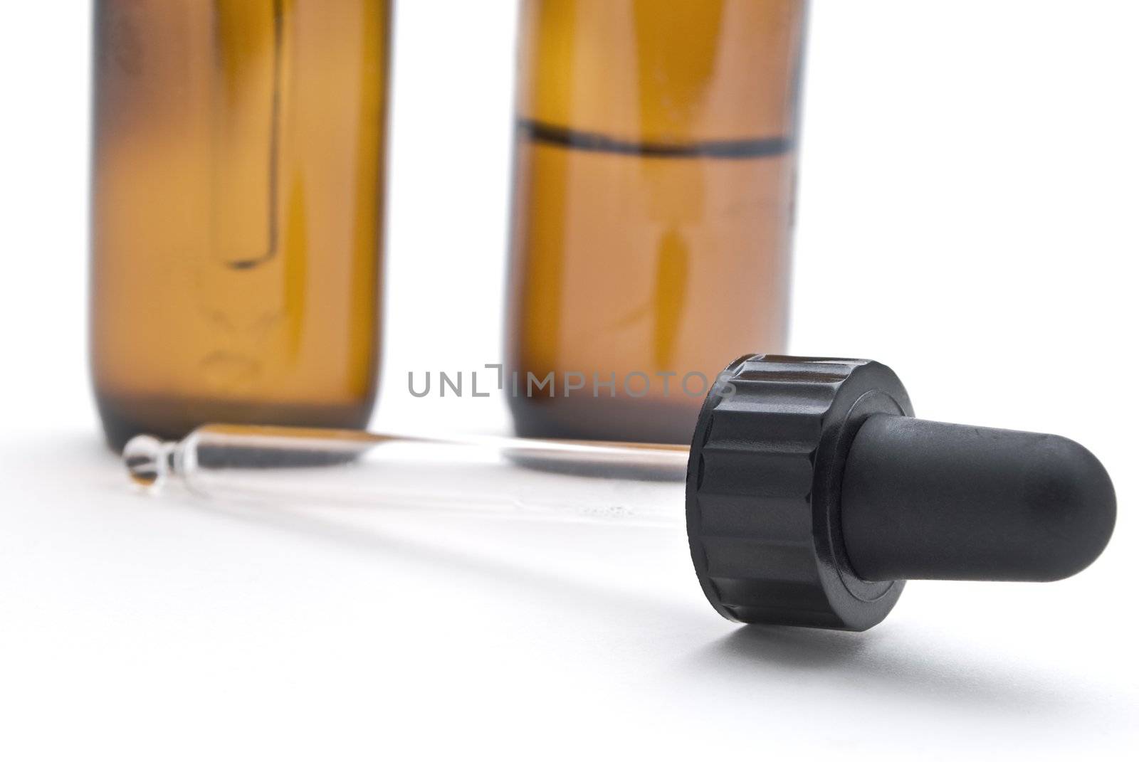 One glass pipette, lying on a white surface in the foreground, with two amber glass tincture bottles in the background.  Shallow depth of field.