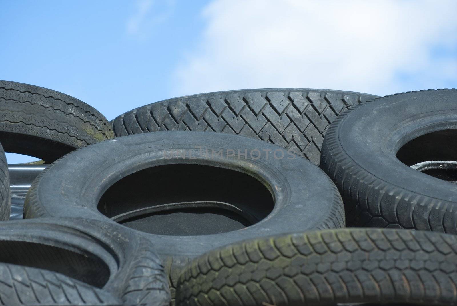 Car Tyres in Recycle Pile against Blue Sky by frannyanne