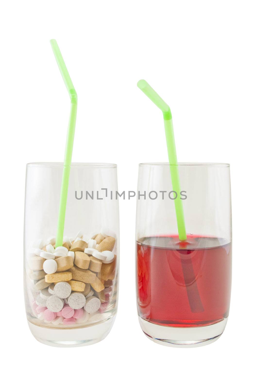 A glass of varied vitamin pills containing a green straw, next to a glass of red berry juice. Isolated against a white background.