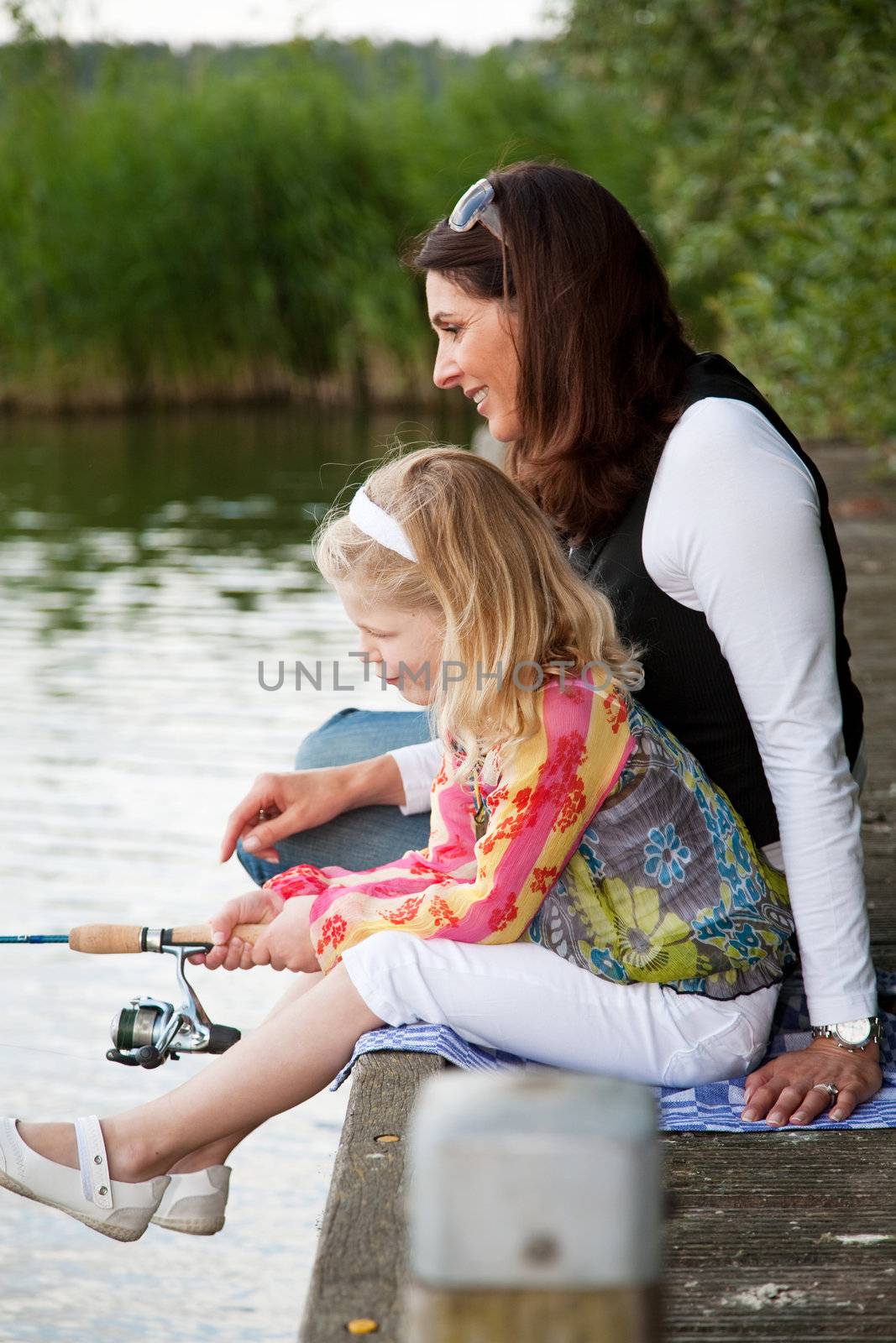 Young girl by the waterside with her mom trying to catch a fish