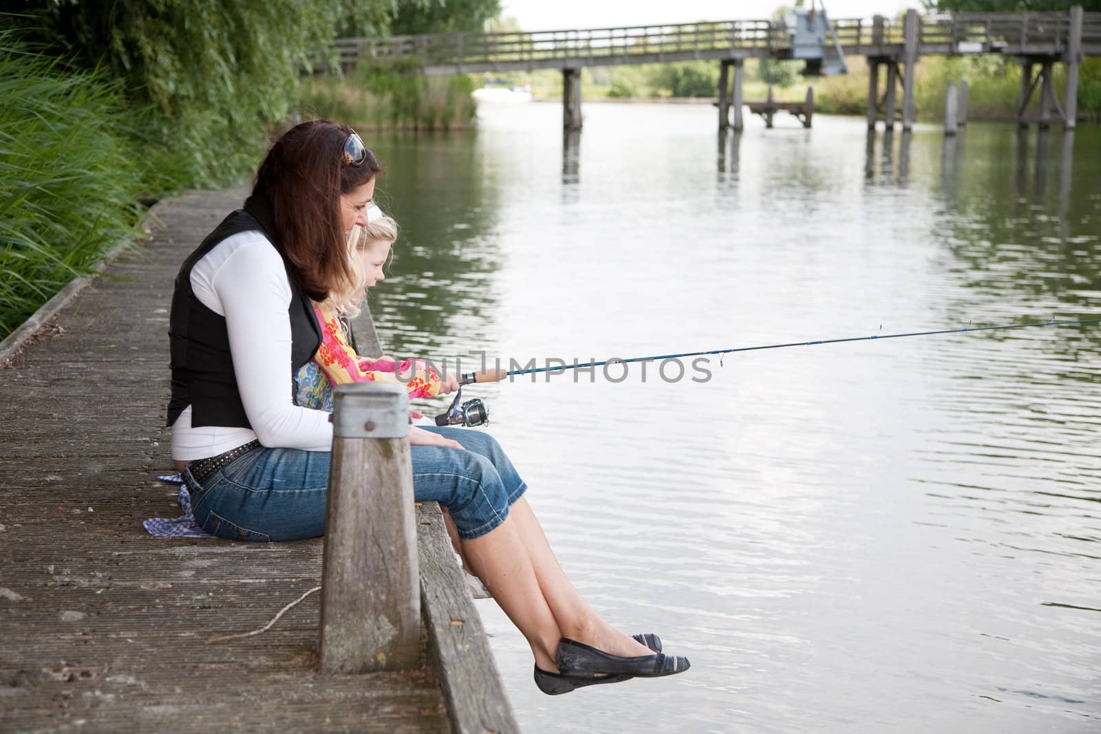 Mom and daughter together by the waterside fishing