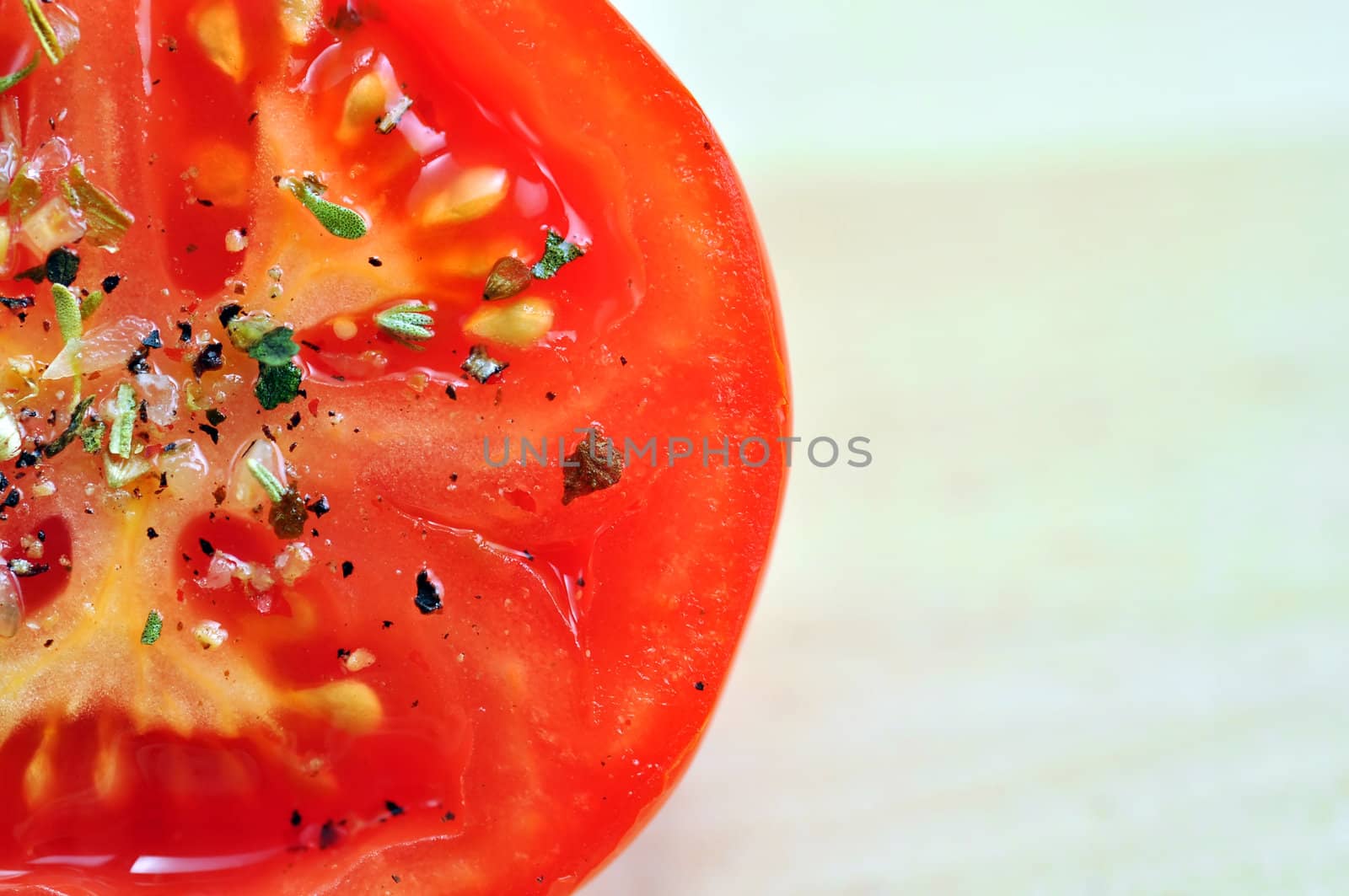 Mouth watering seasoned tomato slice with details on sea salt and herbs, and wooden cutting board background.