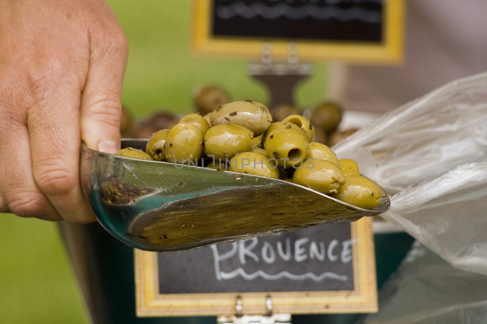 a scoop of herb de provence olives being put into a bag for a customer at a market stall