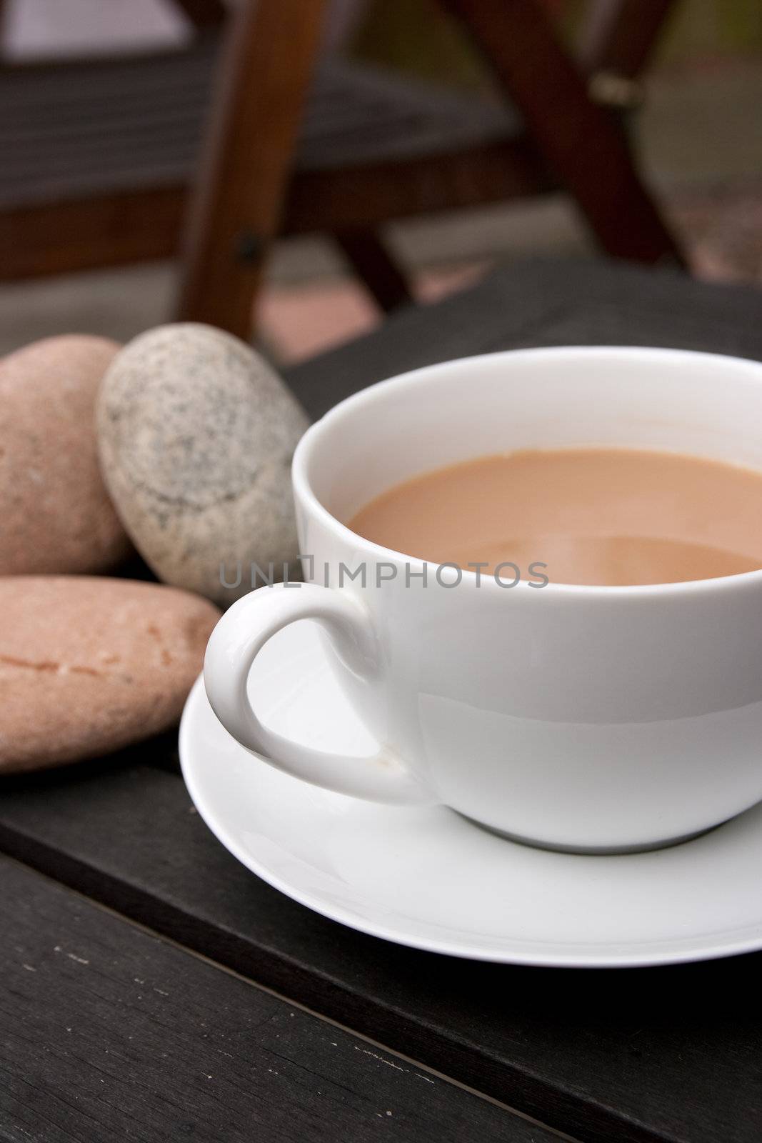 Outdoor cup of tea in a white cup and saucer with stones on a wooden background