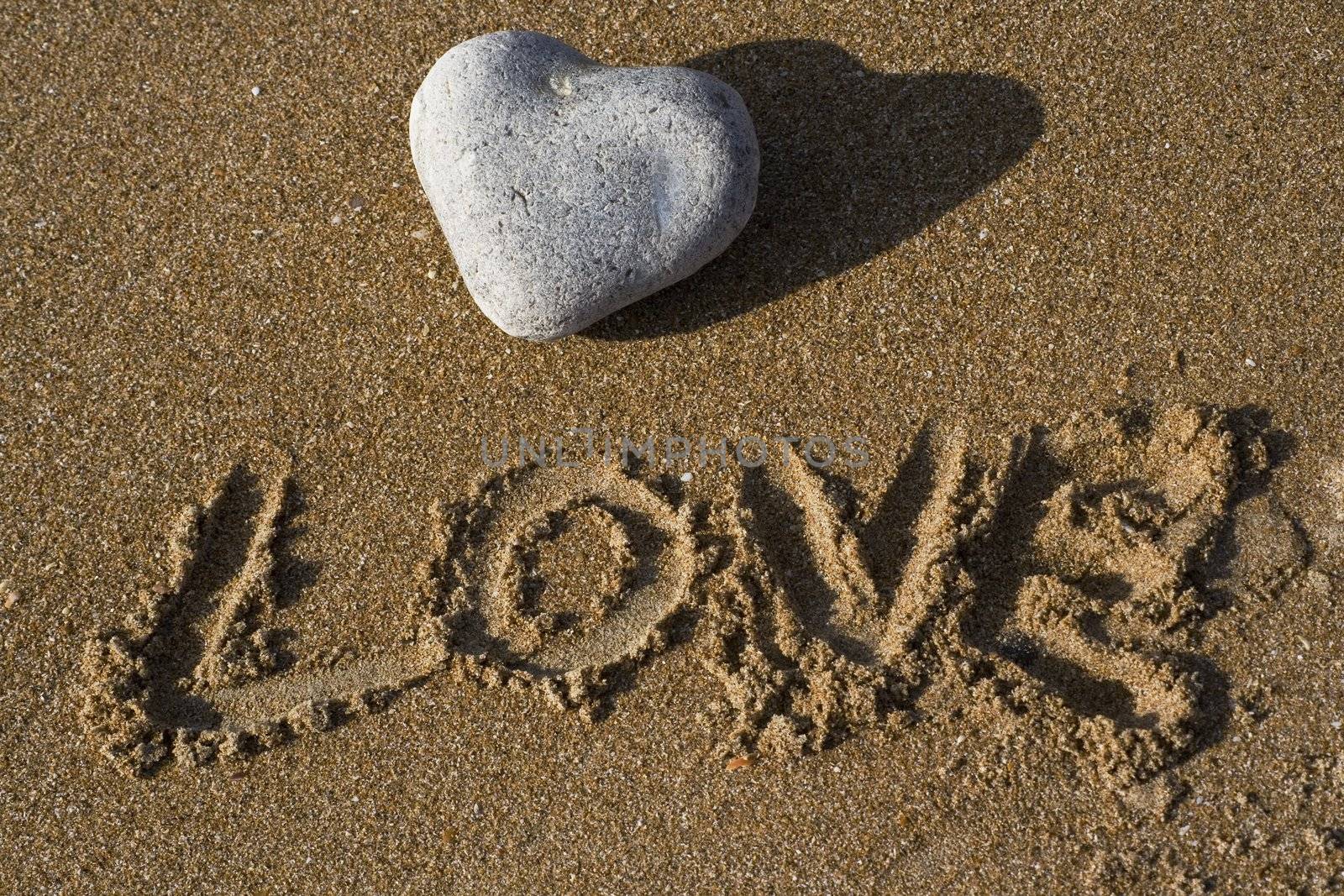 A heart shaped stone on a sandy beach with the word love under written in the sand