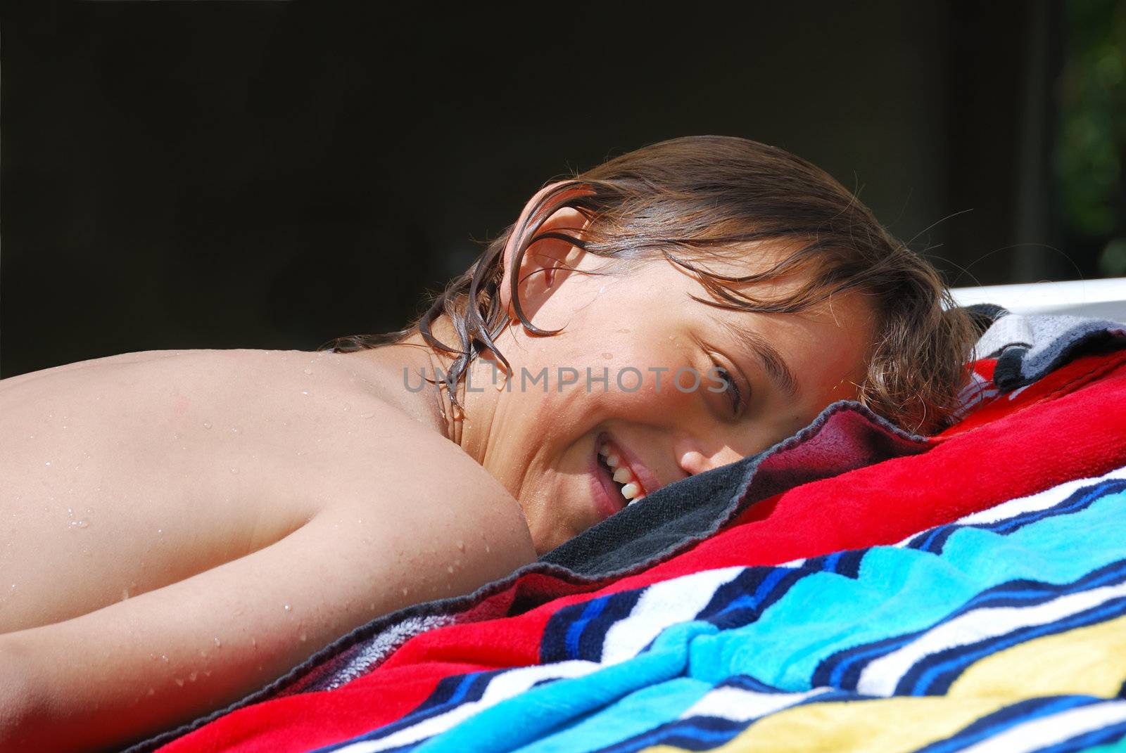 Smiling teen boy lying down on a beach towel and sunbathing.