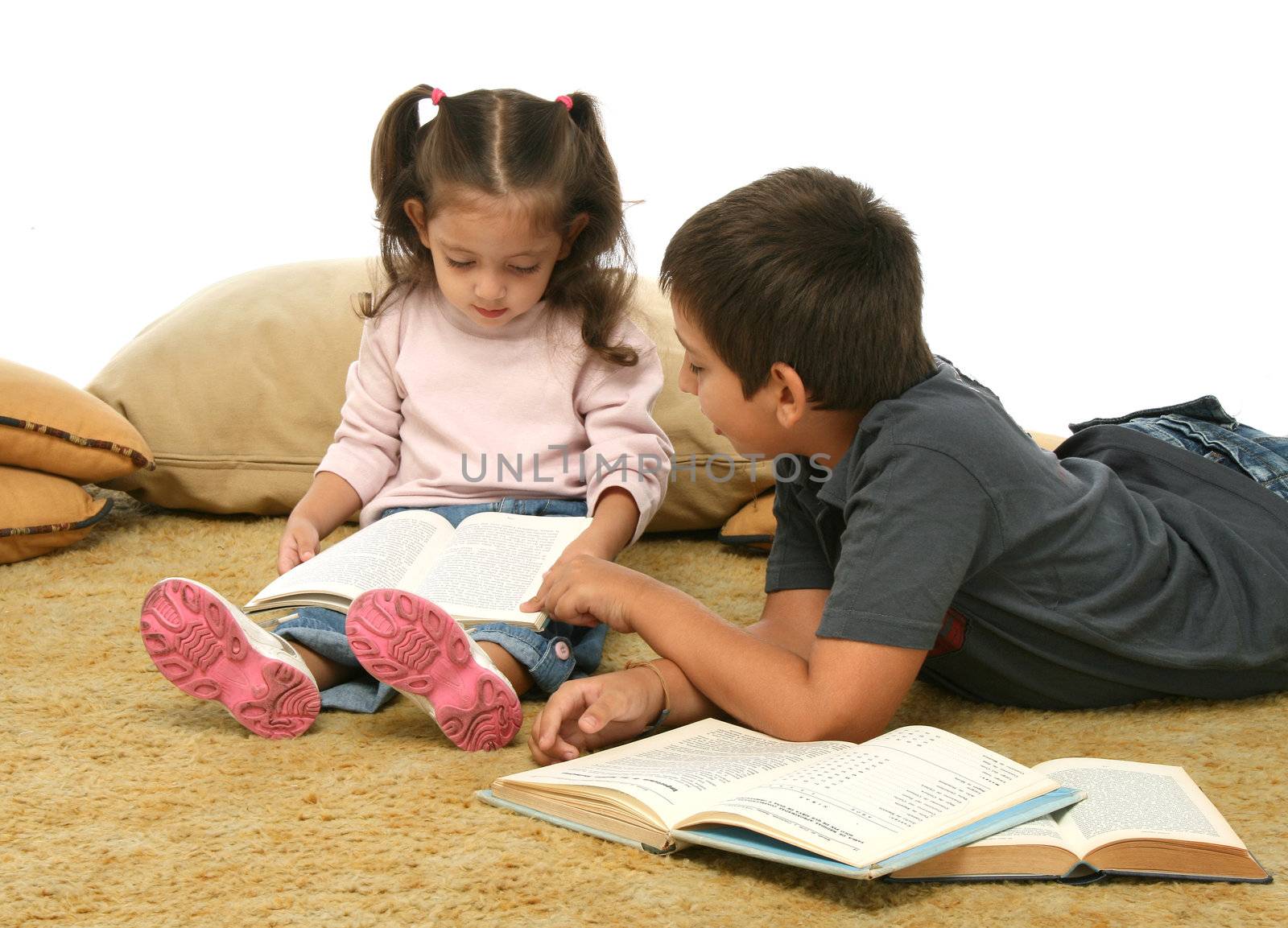 Brother and sister reading books over a carpet. They look interested and concentrated. 
