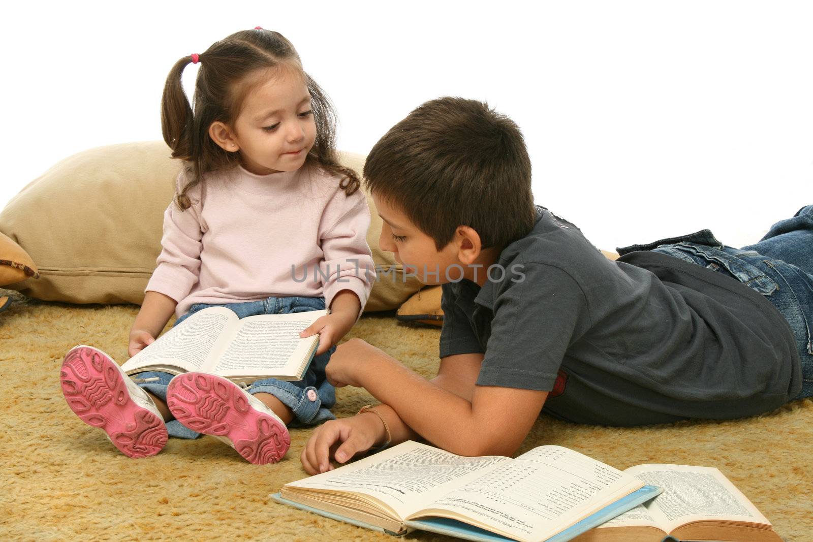 Brother and sister reading books over a carpet. They look interested and concentrated. 
