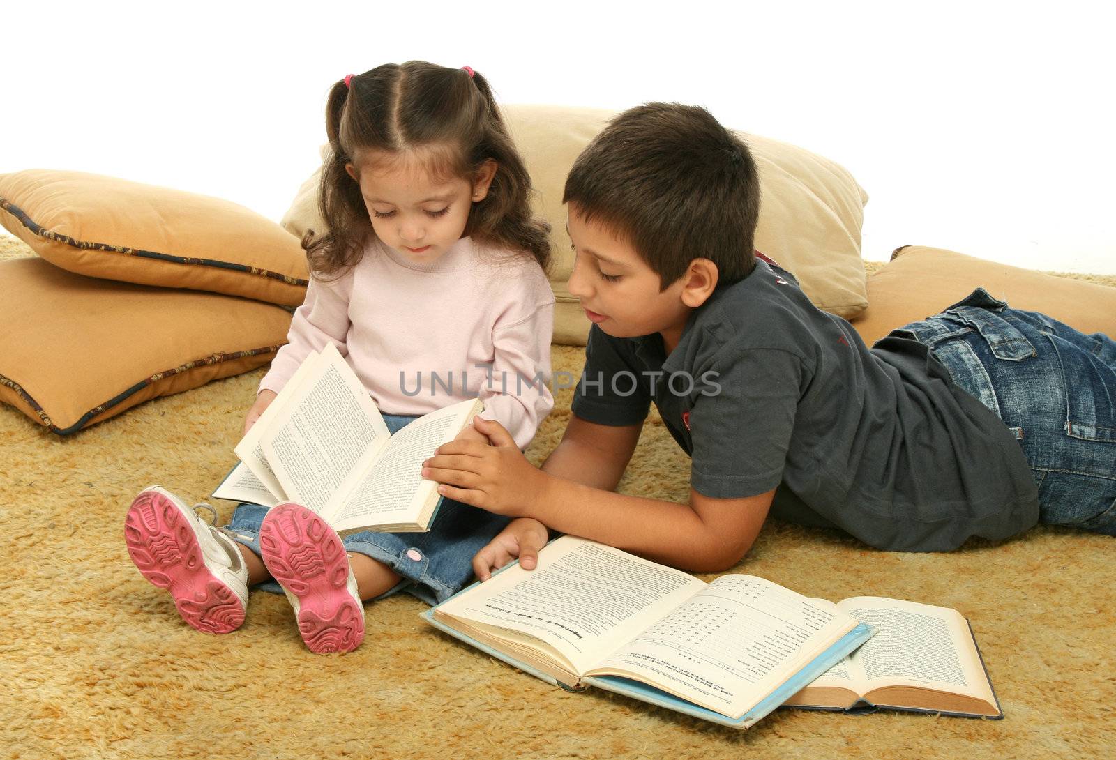 Brother and sister reading books over a carpet. They look interested and concentrated. 
