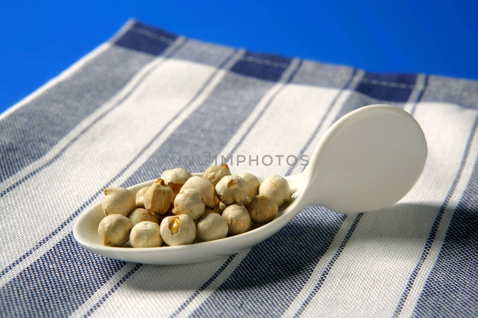 Chickpeas toasted on a white porcelain spoon over blue