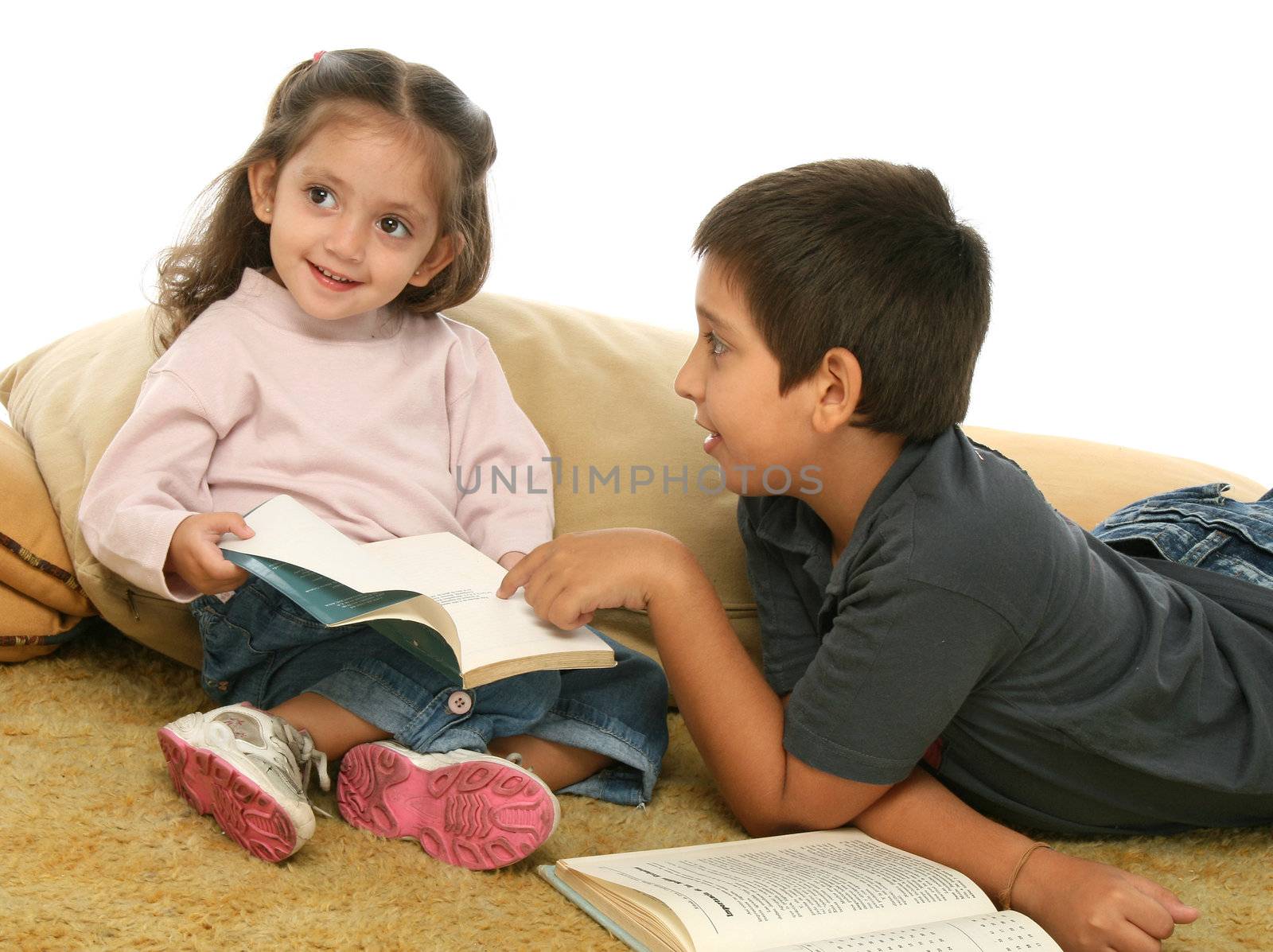 Brother and sister reading books over a carpet. They look interested and concentrated. 
