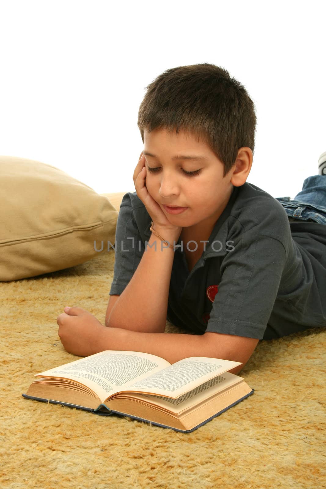 Boy in a room reading a book over a carpet. 