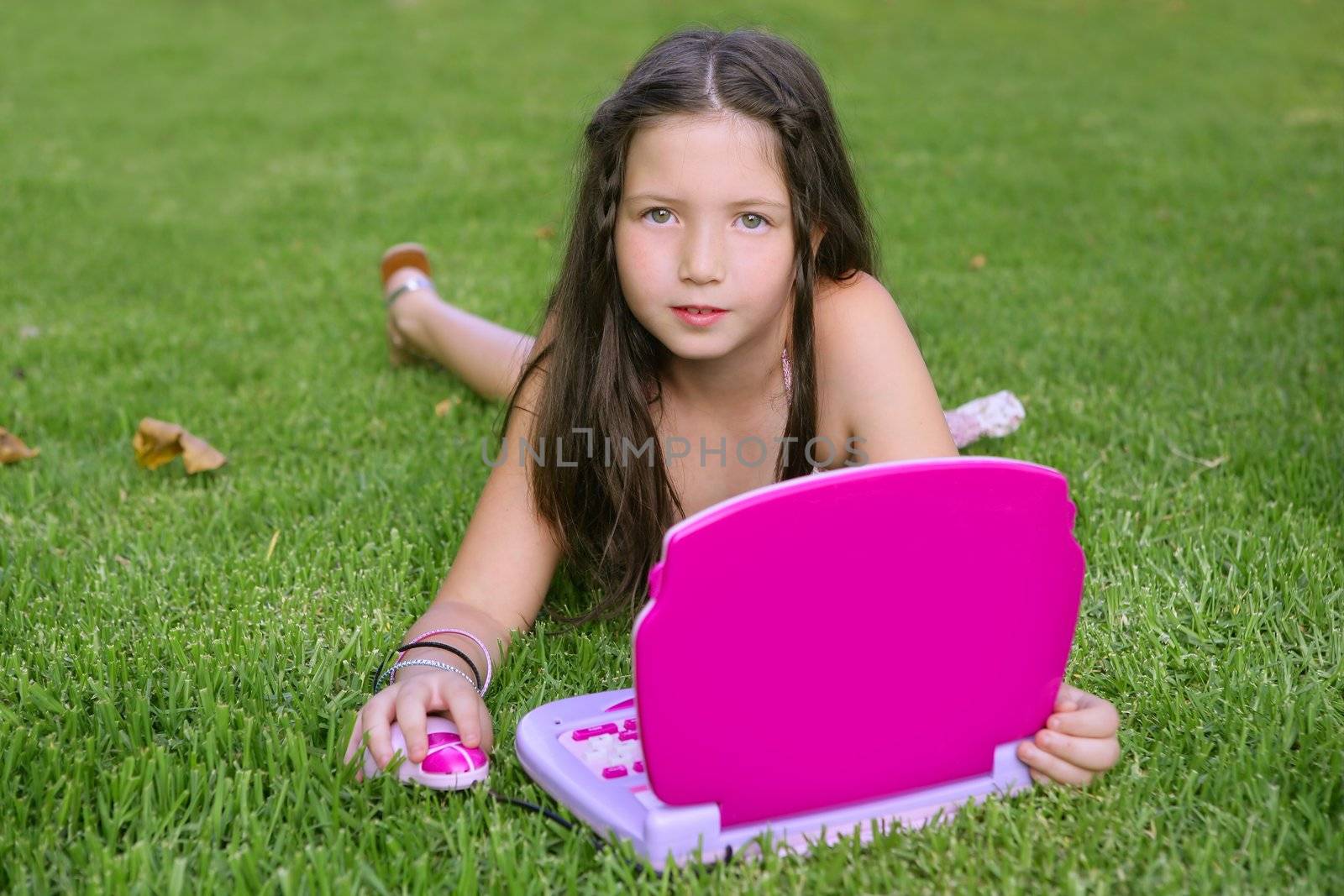 Beautiful little girl playing with pink toy computer outdoor in grass