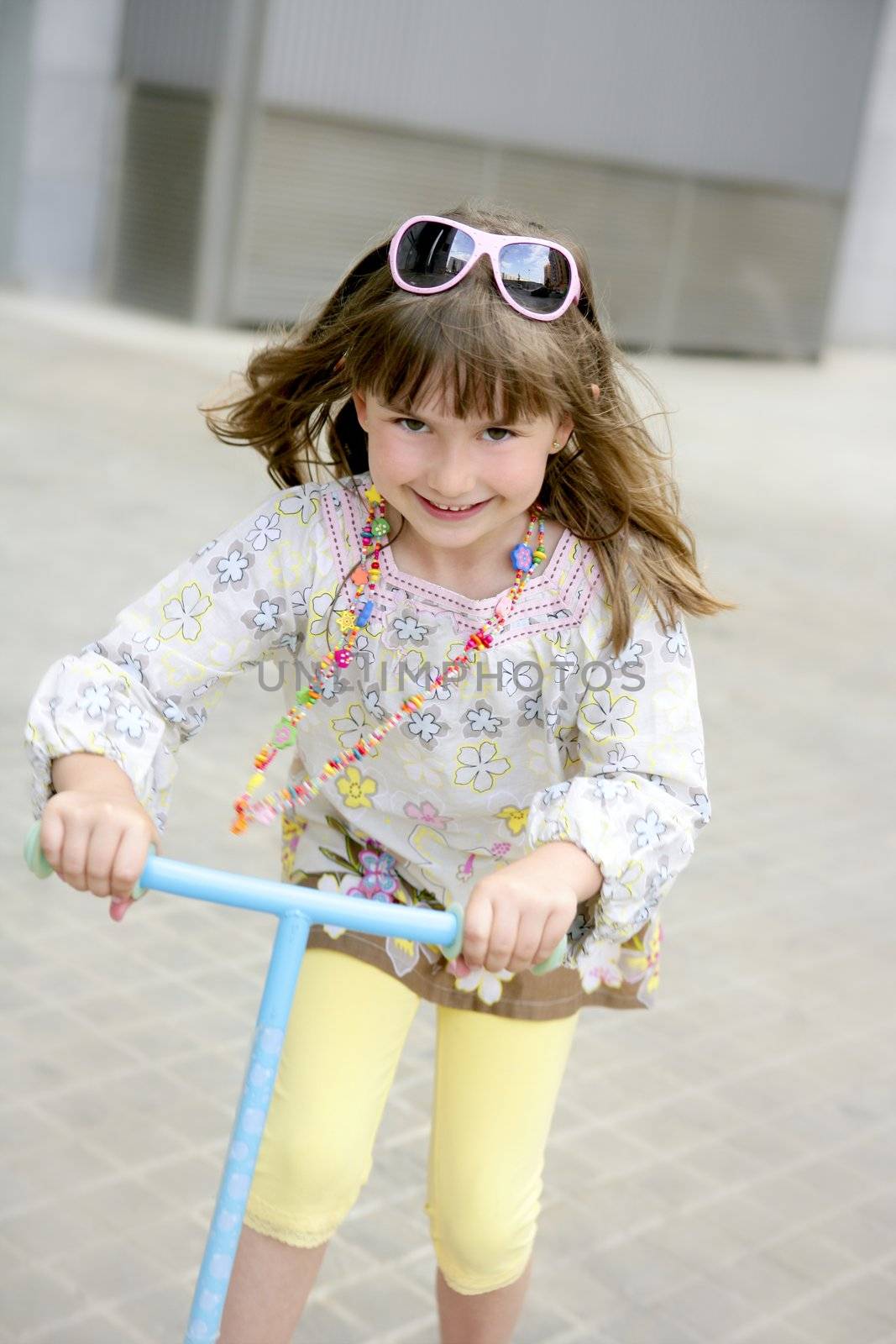 Brunette little girl with scooter in gray city background