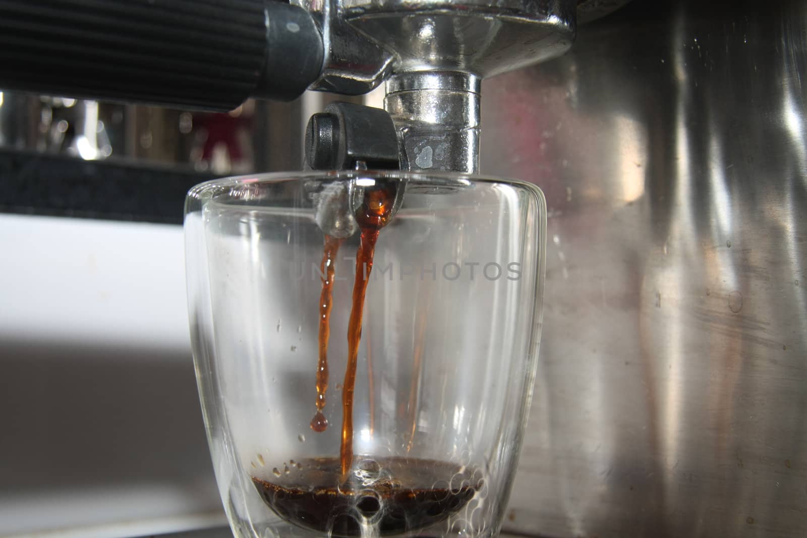 A glass in close up under a traditional italian espresso maker
