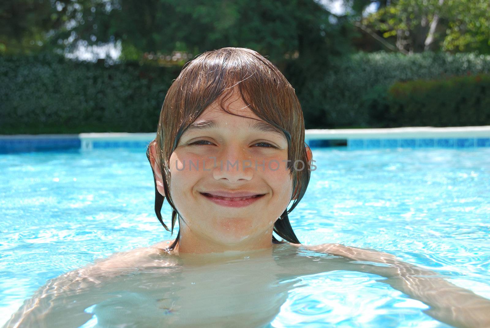 Smiling teenage boy swimming in the pool surrounded with white flower bushes in the background.