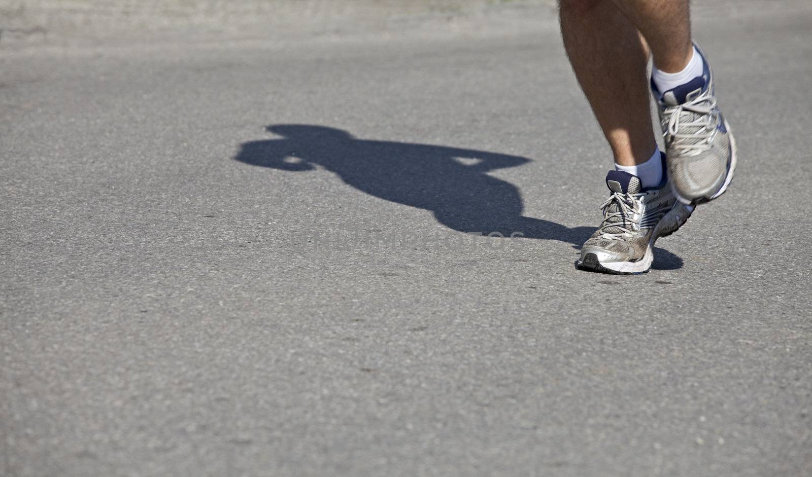 feet and shadow of a jogger on asphalt by bernjuer