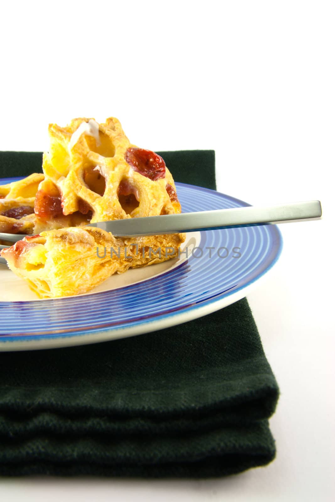 Raspberry and custard danish on a blue and white plate with a fork and black napkin on a white background