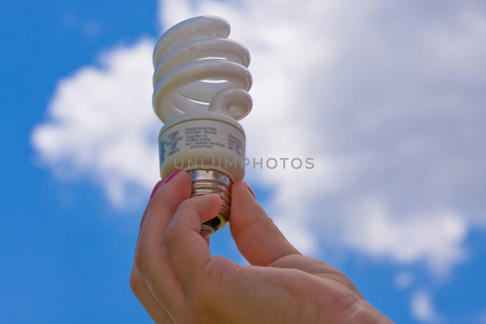 female teen holding a compact fluorescent light bulb up with a cloudy blue sky