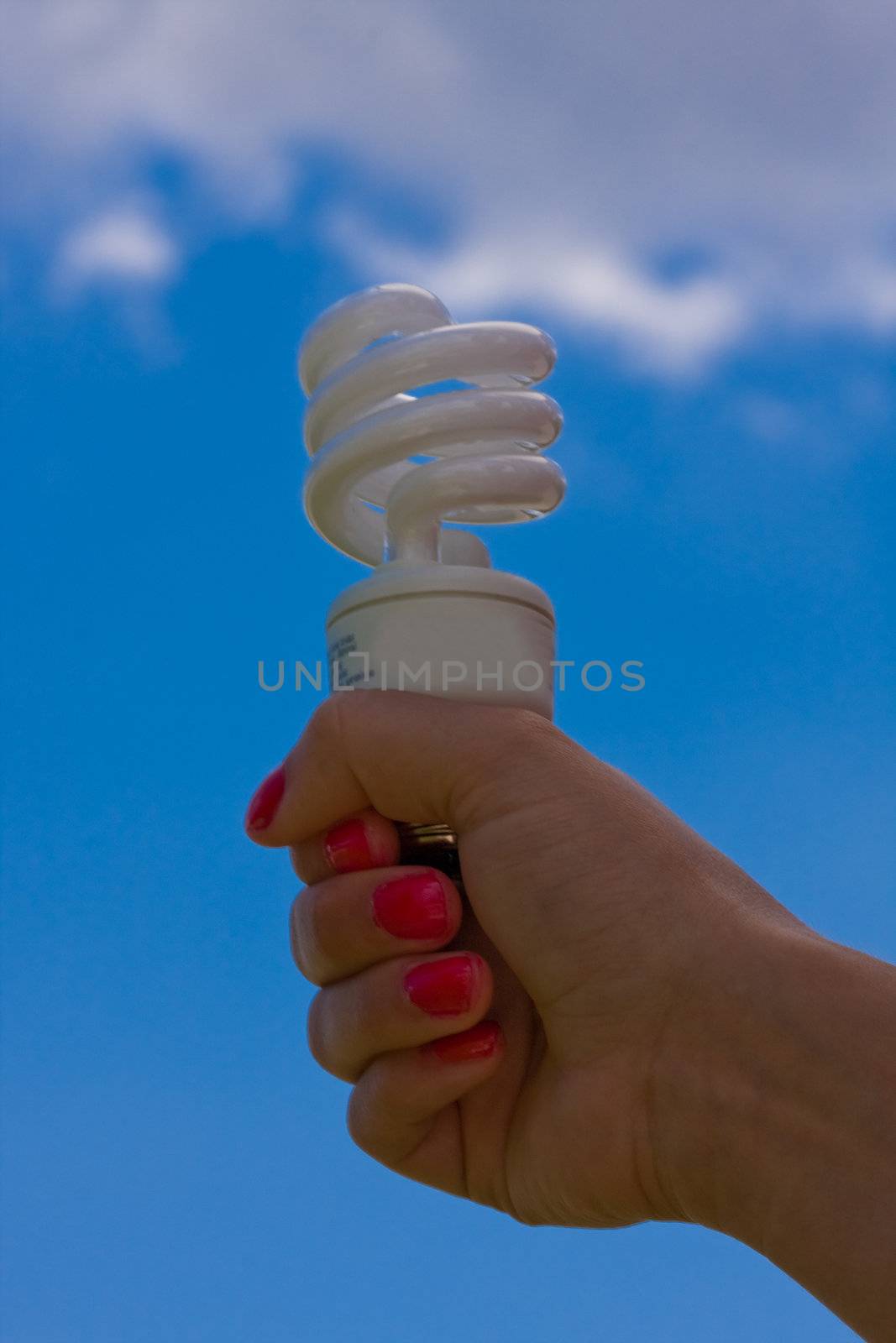 female teen holding a compact fluorescent light bulb up with a cloudy blue sky