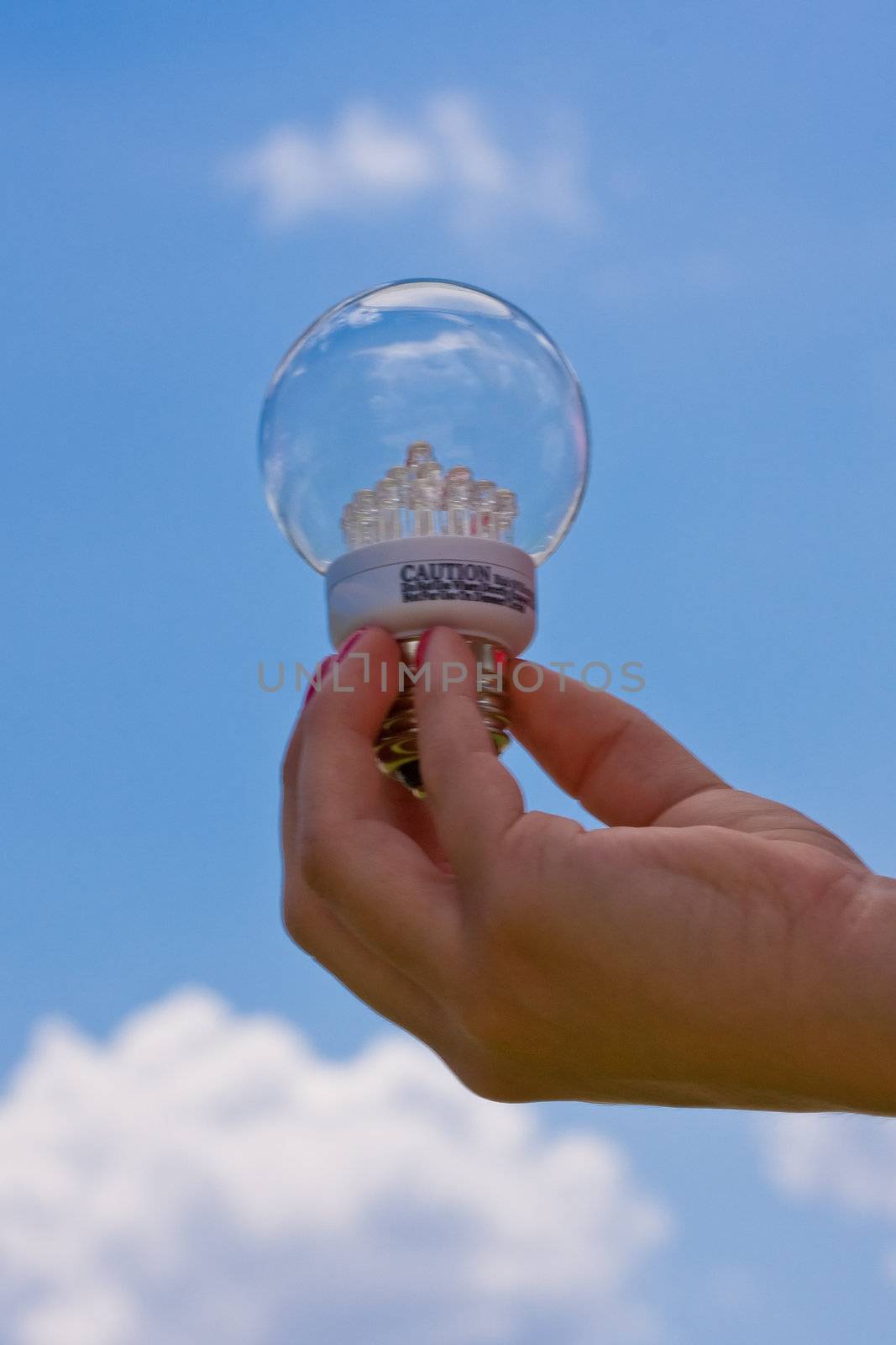 female teen holding a led light bulb up with a cloudy blue sky