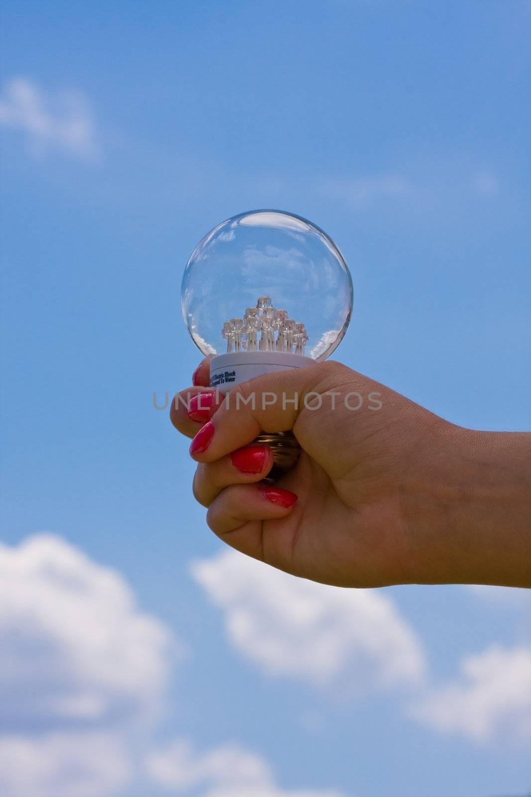 female teen holding a led light bulb up with a cloudy blue sky