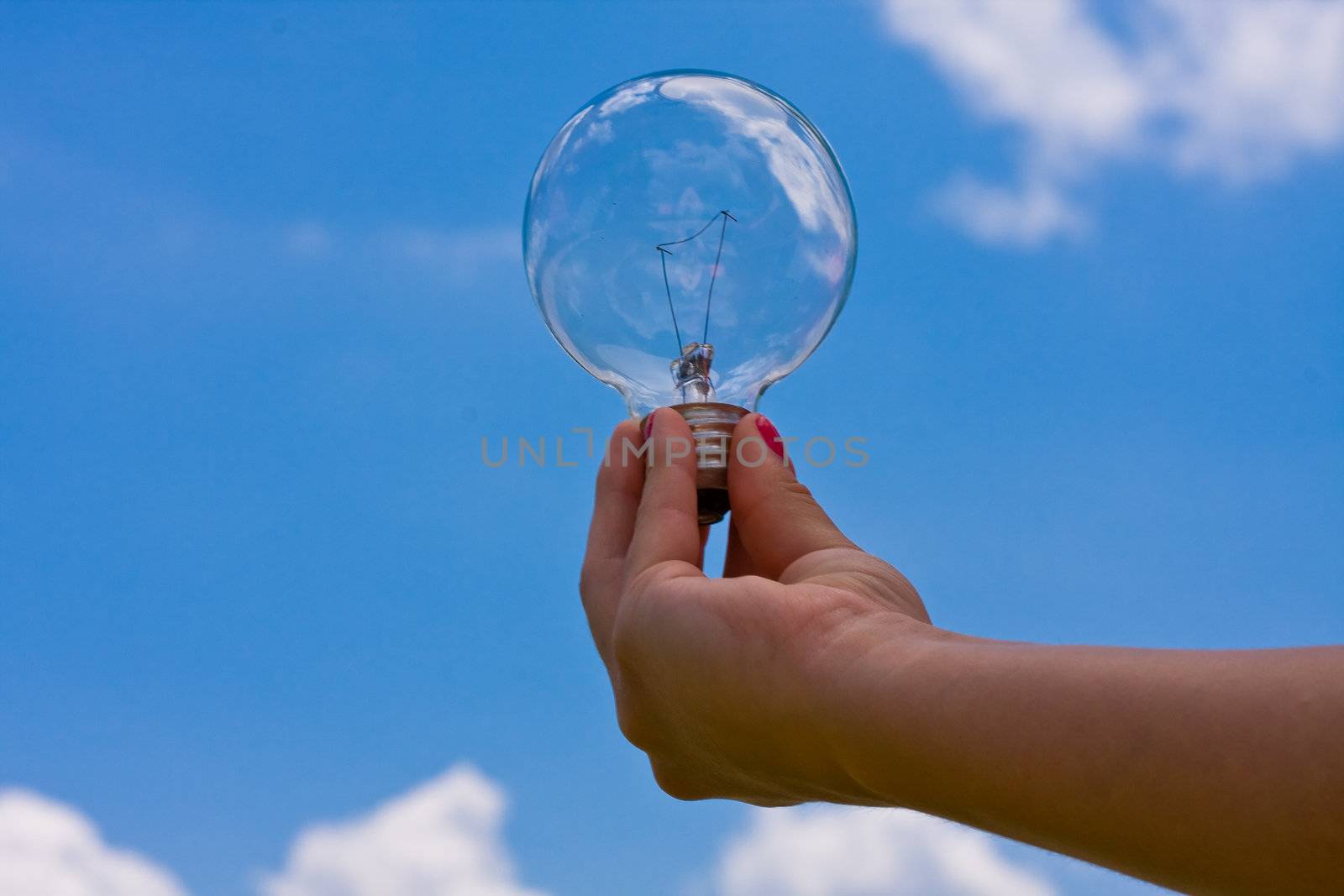 female teen holding a light bulb up with a cloudy blue sky