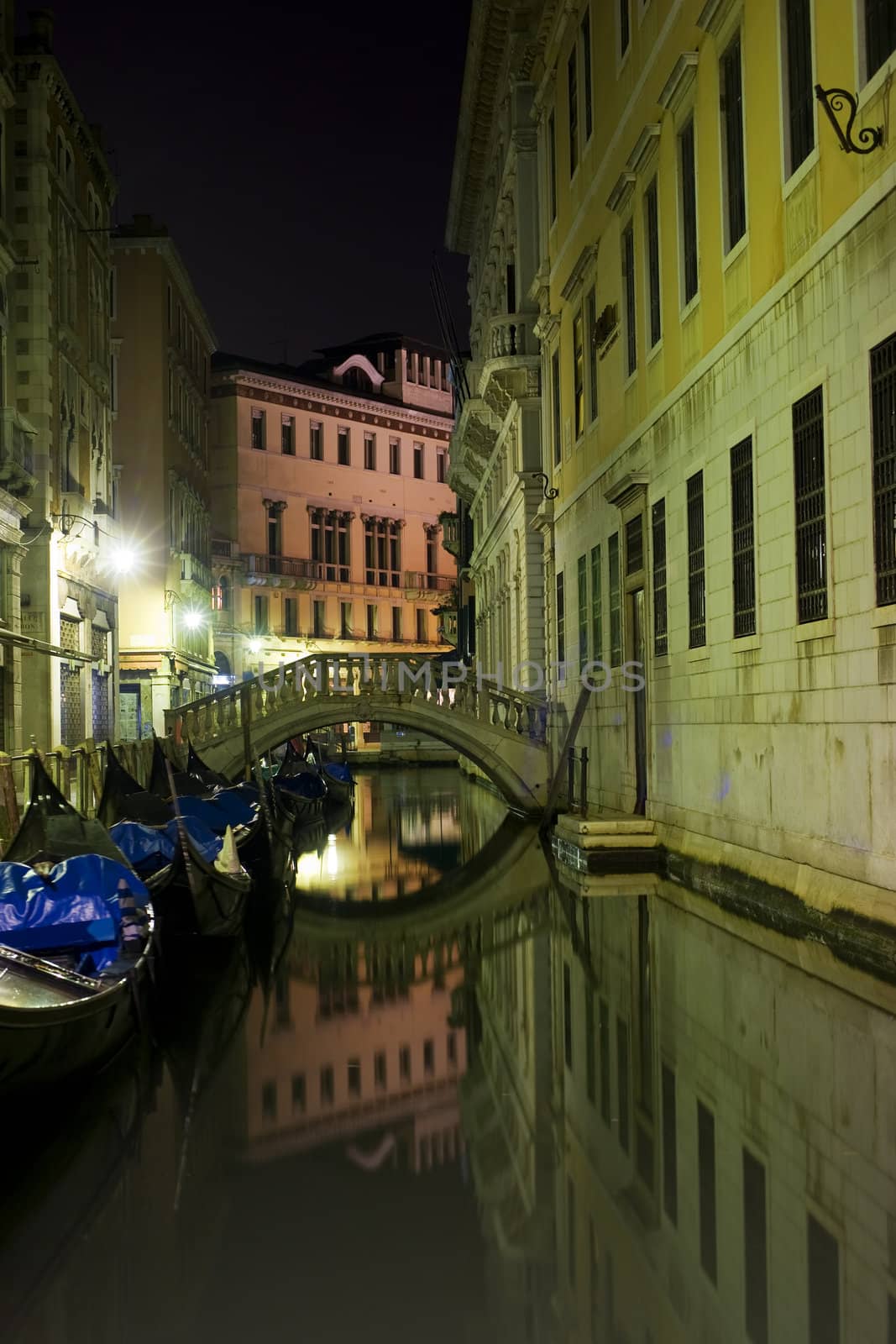 a small canal in the world famous town of Venice. In the foreground some typical boats and in the background a small bridge.