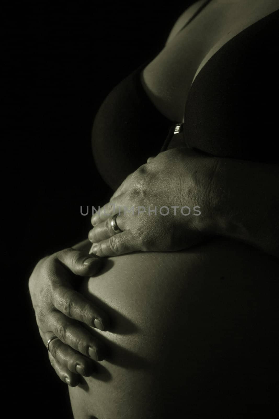 Two hands of a pregnant woman touching her skin