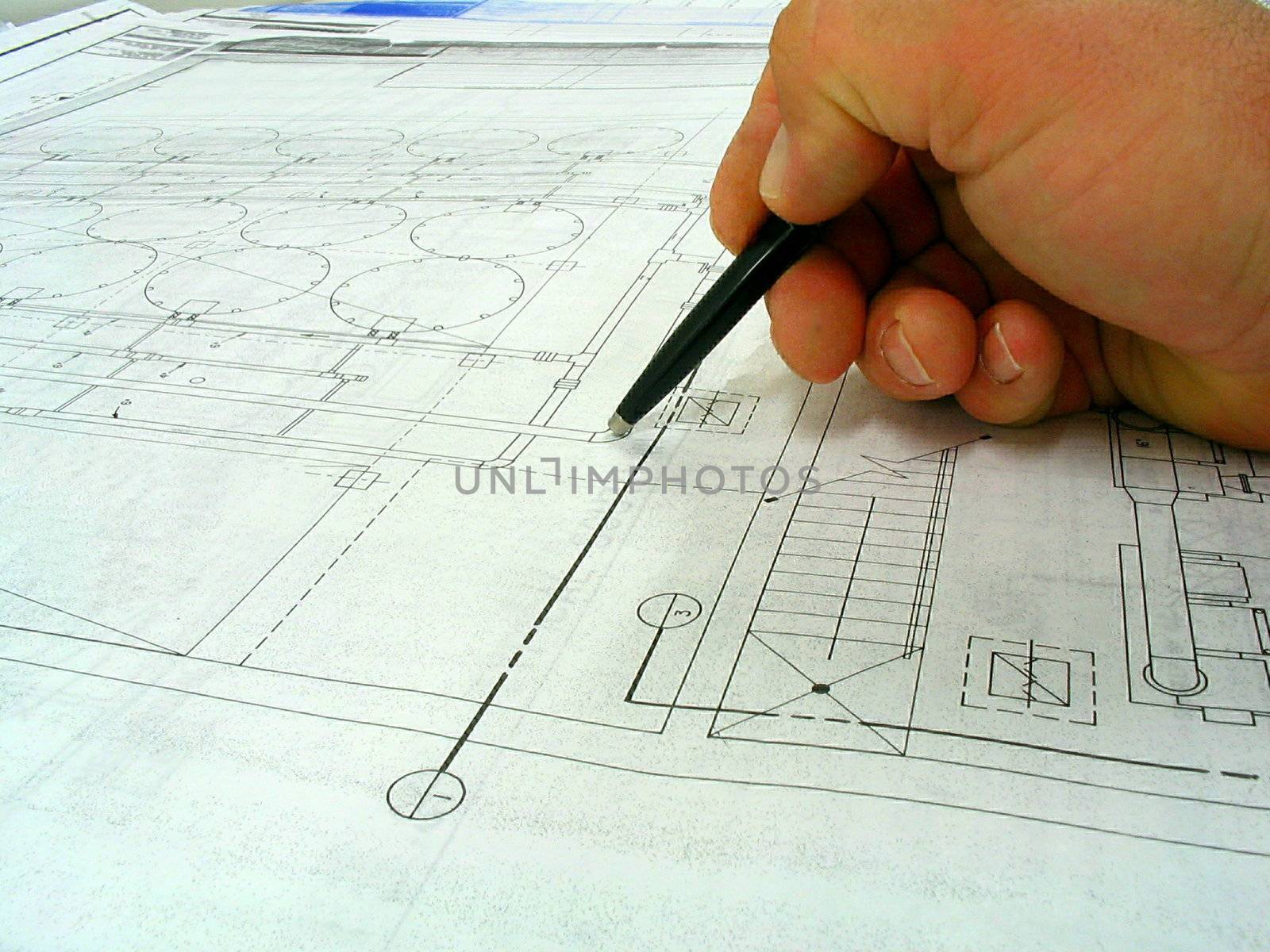 This is a drafters hand with pen carefully looking over a black line drawing. 