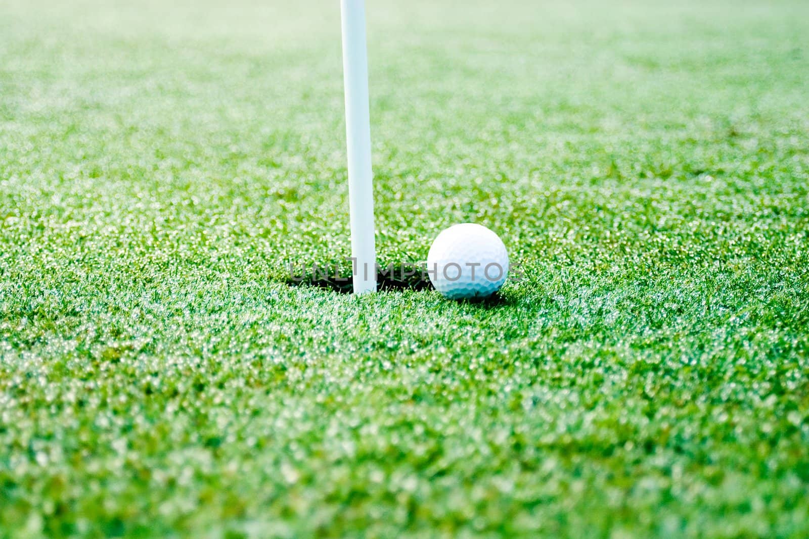 This is a picture of a golf ball next to the hole with flag pole showing. slective focus is on the ball and hole.