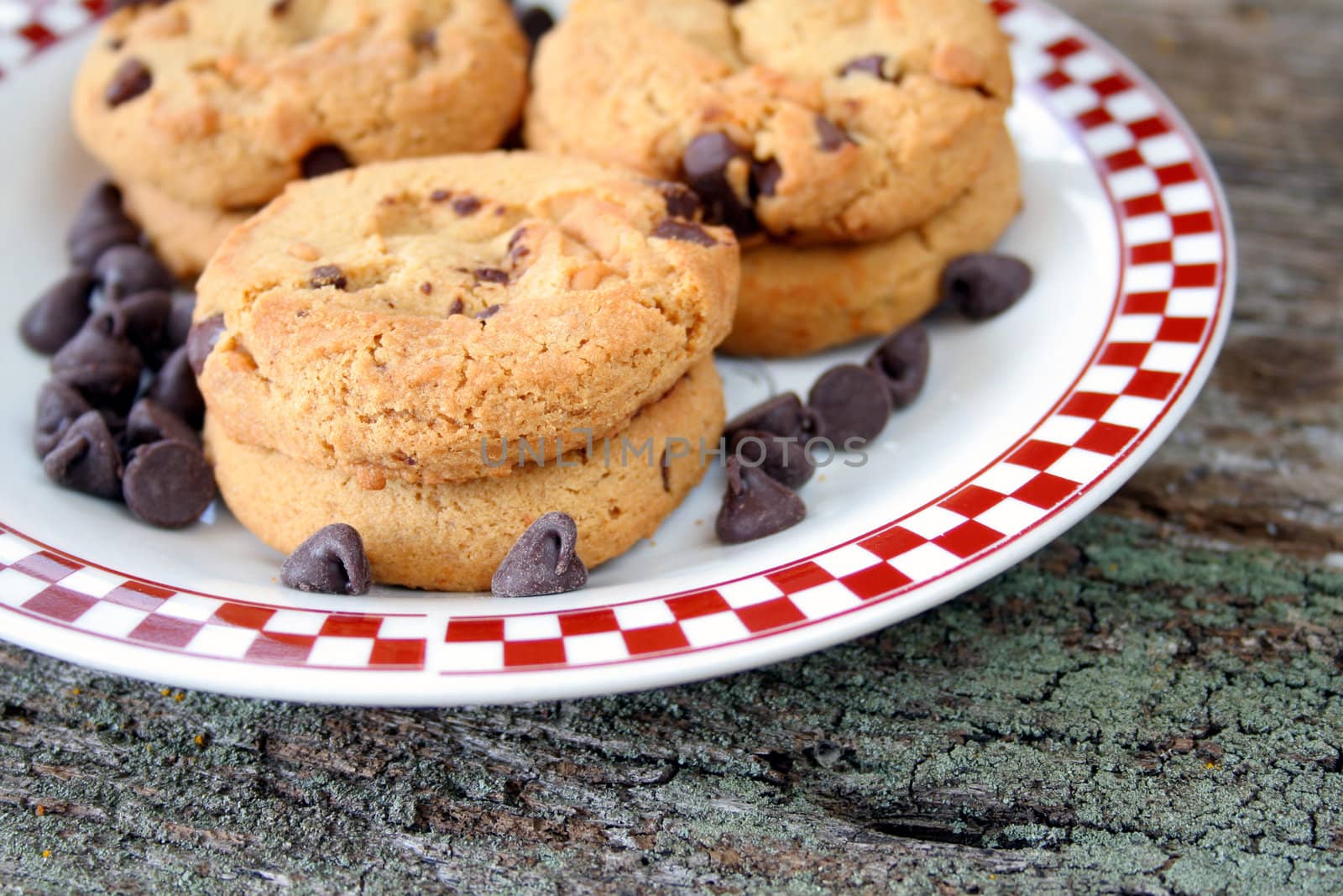 Chocolate chip cookies on a plate with chocolate chips laying around the cookies.