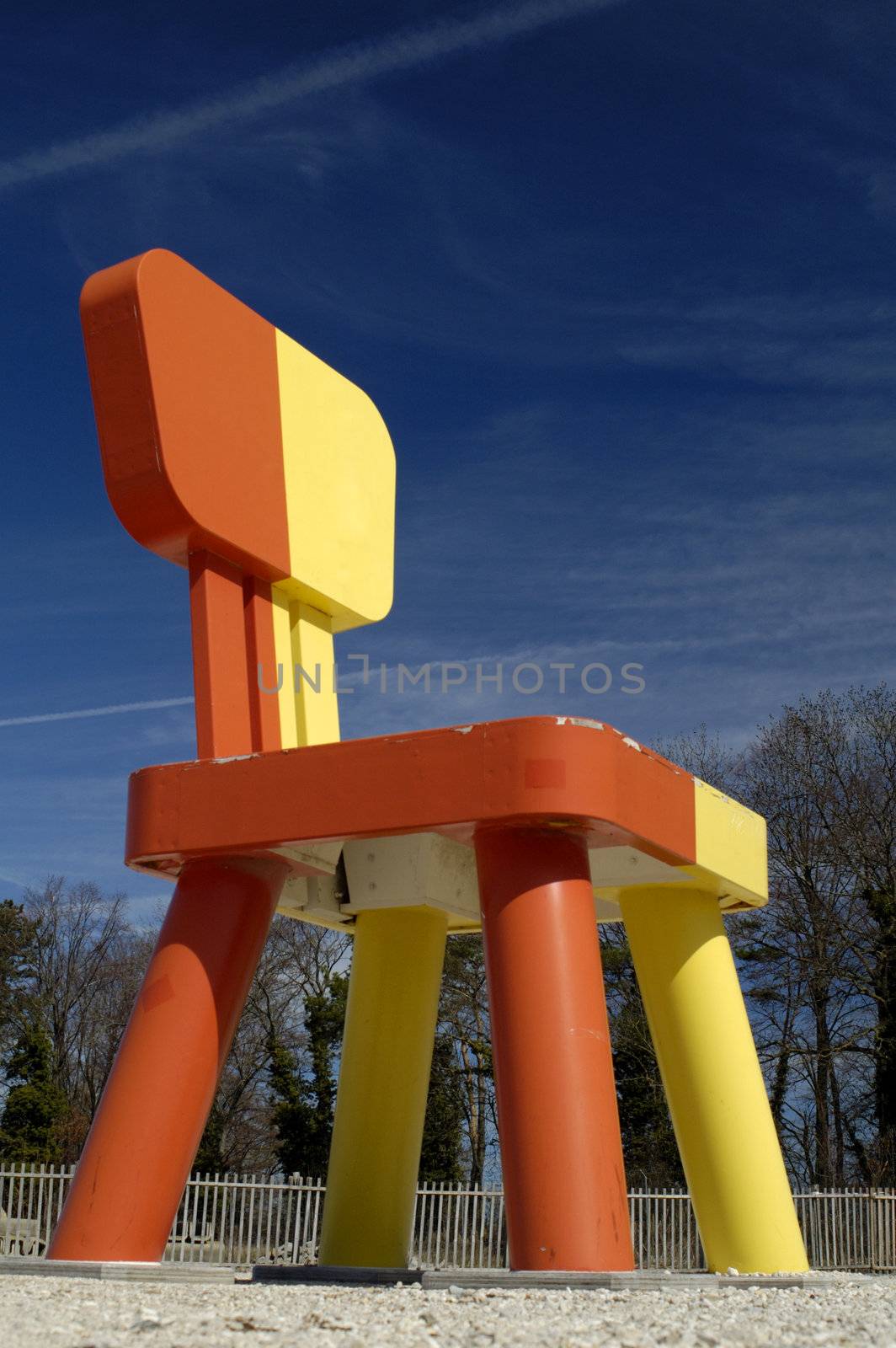 A huge chair towers over trees and a wooden fence, against a rich blue sky.