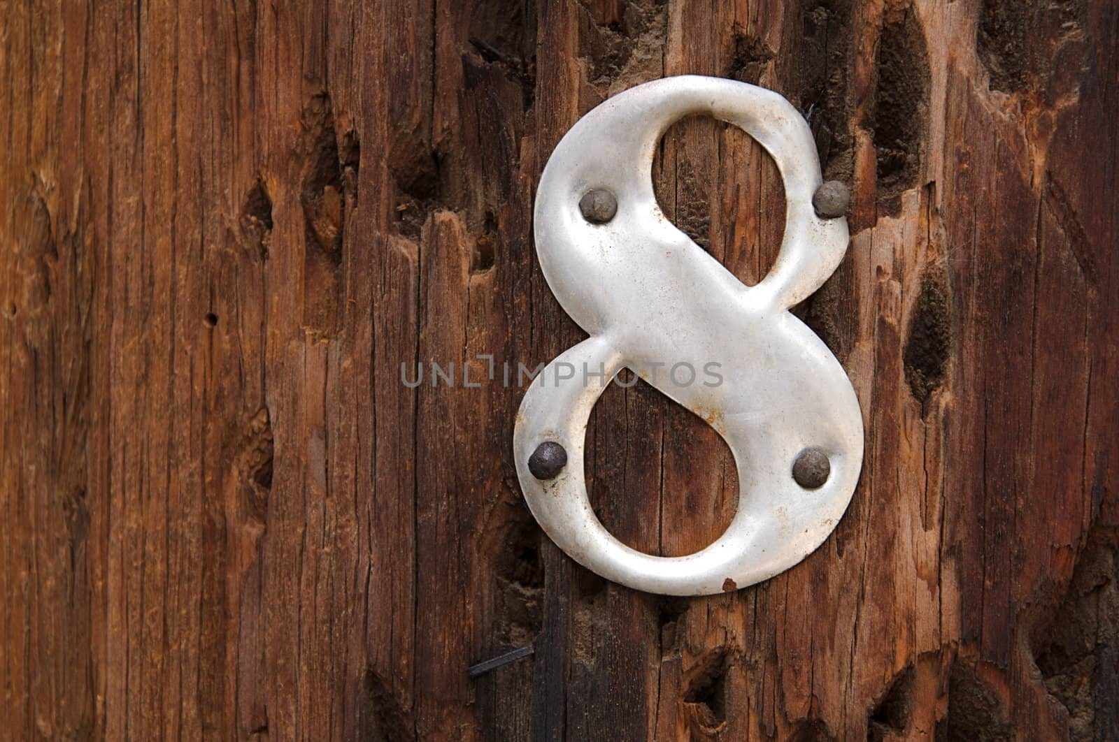 A metal number 8 is attached to a rough, worn telephone pole.